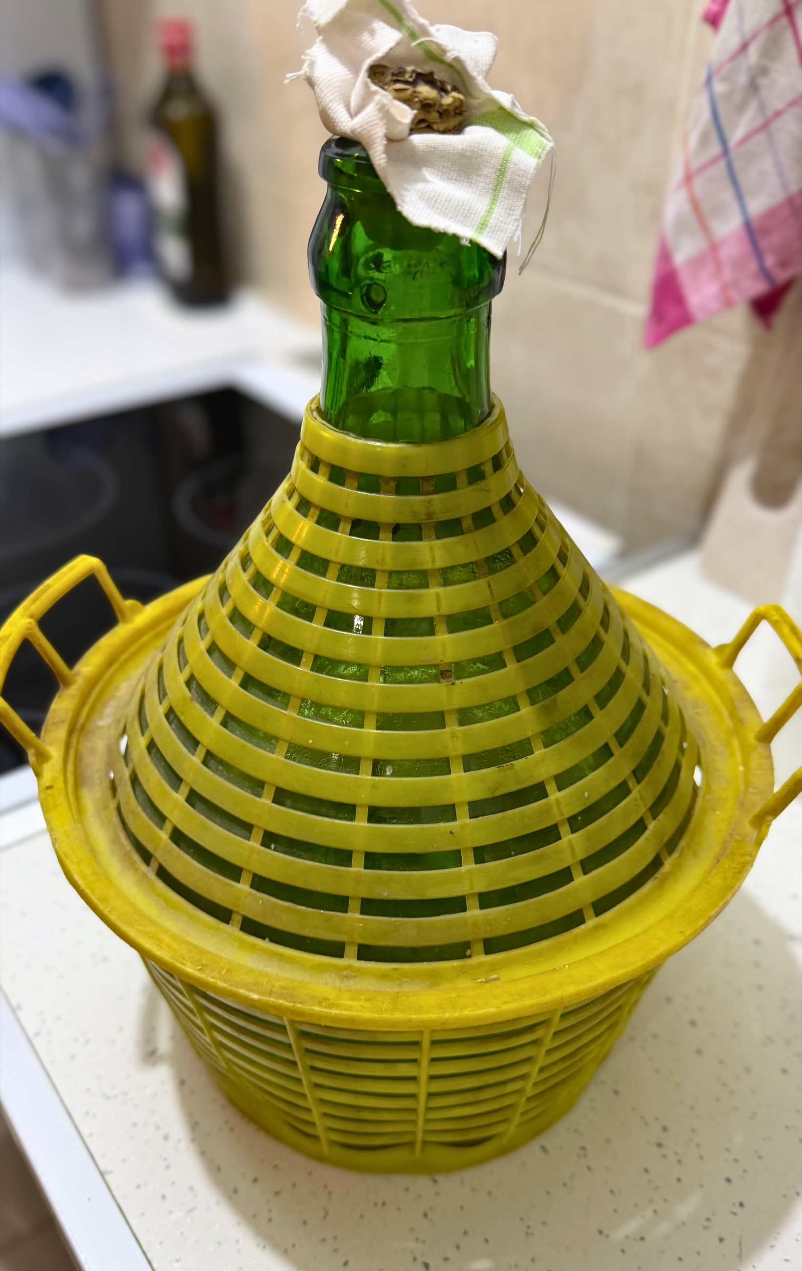 A large glass jug of homemade grape rakija in a woven basket on the apartment kitchen counter.