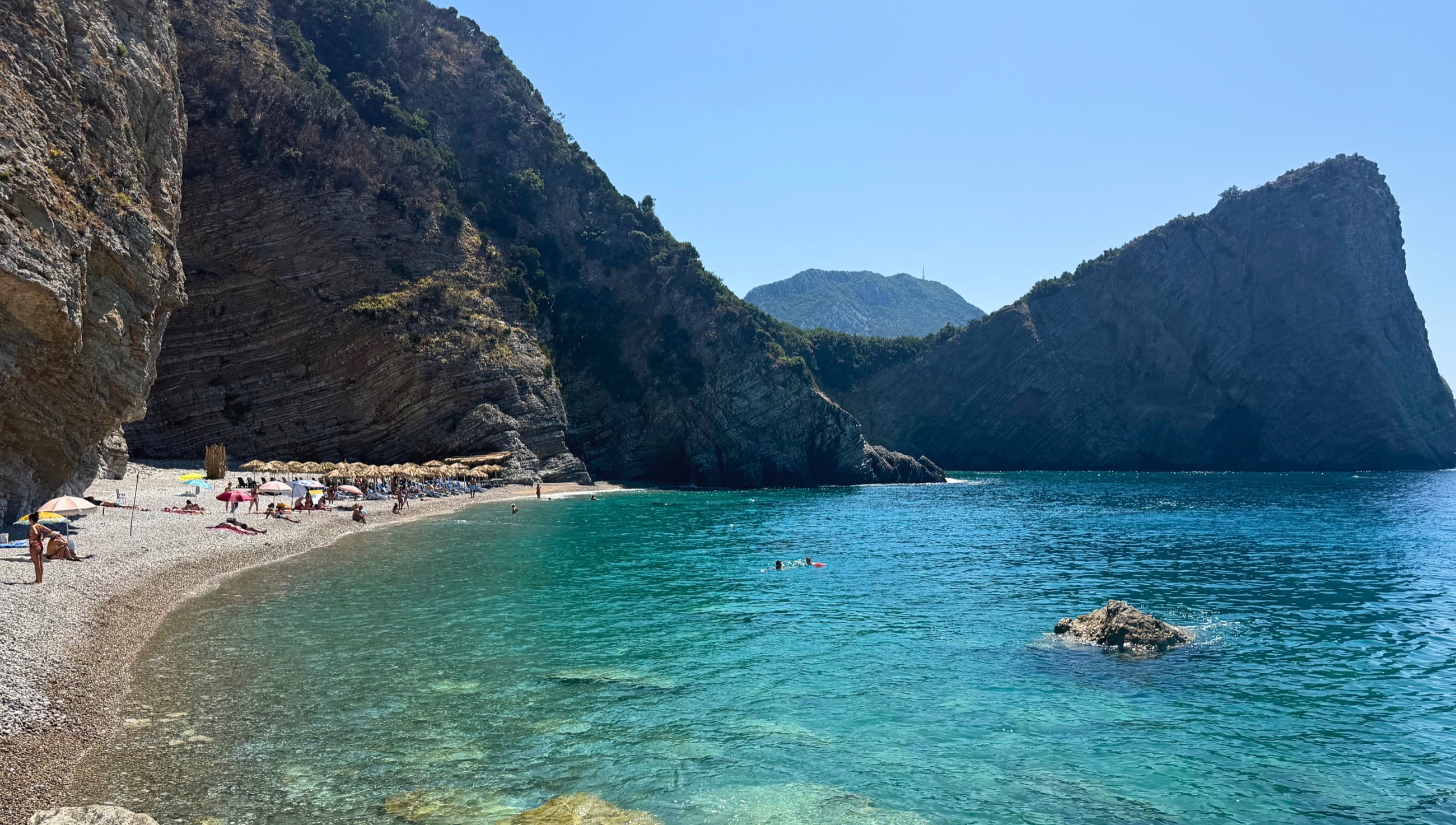 Vezirova Beach near Čanj, with clear blue water enclosed by steep folded cliffs.