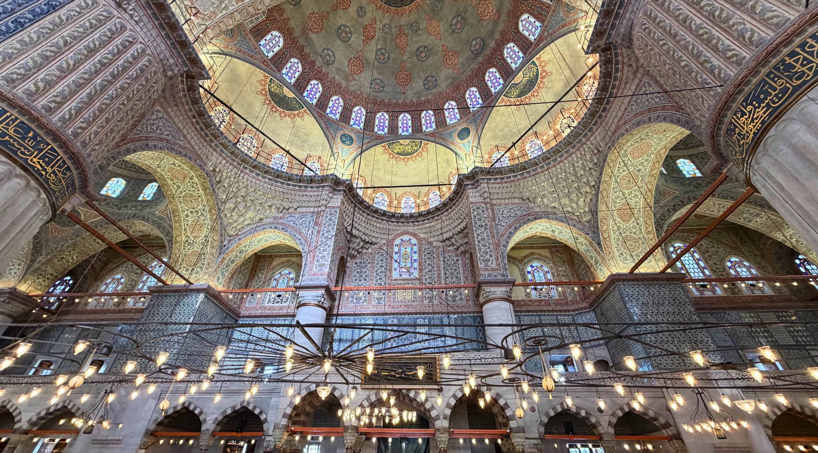 The interior of the Blue Mosque with patterned domes, arches, hanging lights, and blue İznik tiles.