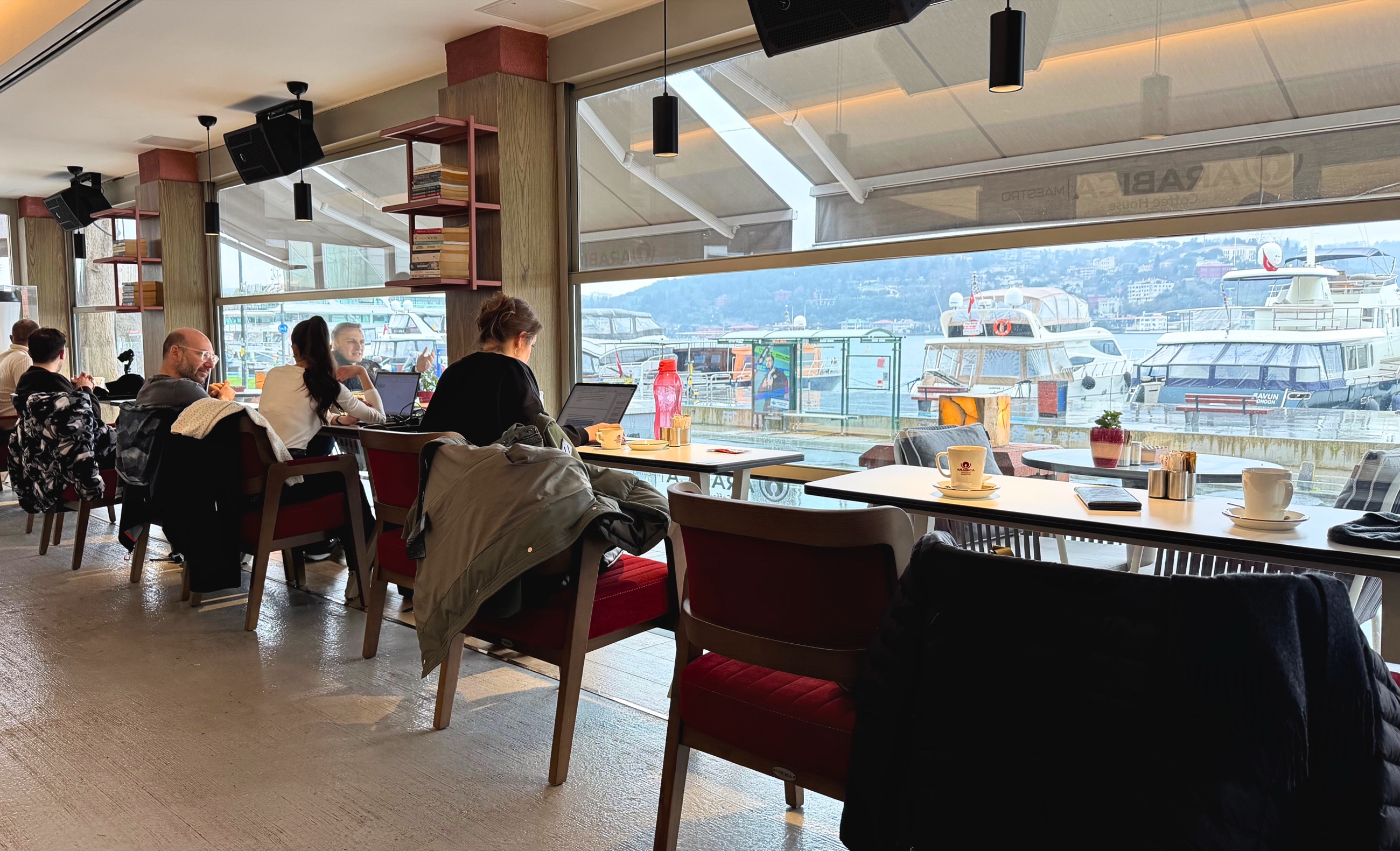 A café interior beside the Bosphorus with tea on the tables and boats visible through the windows.
