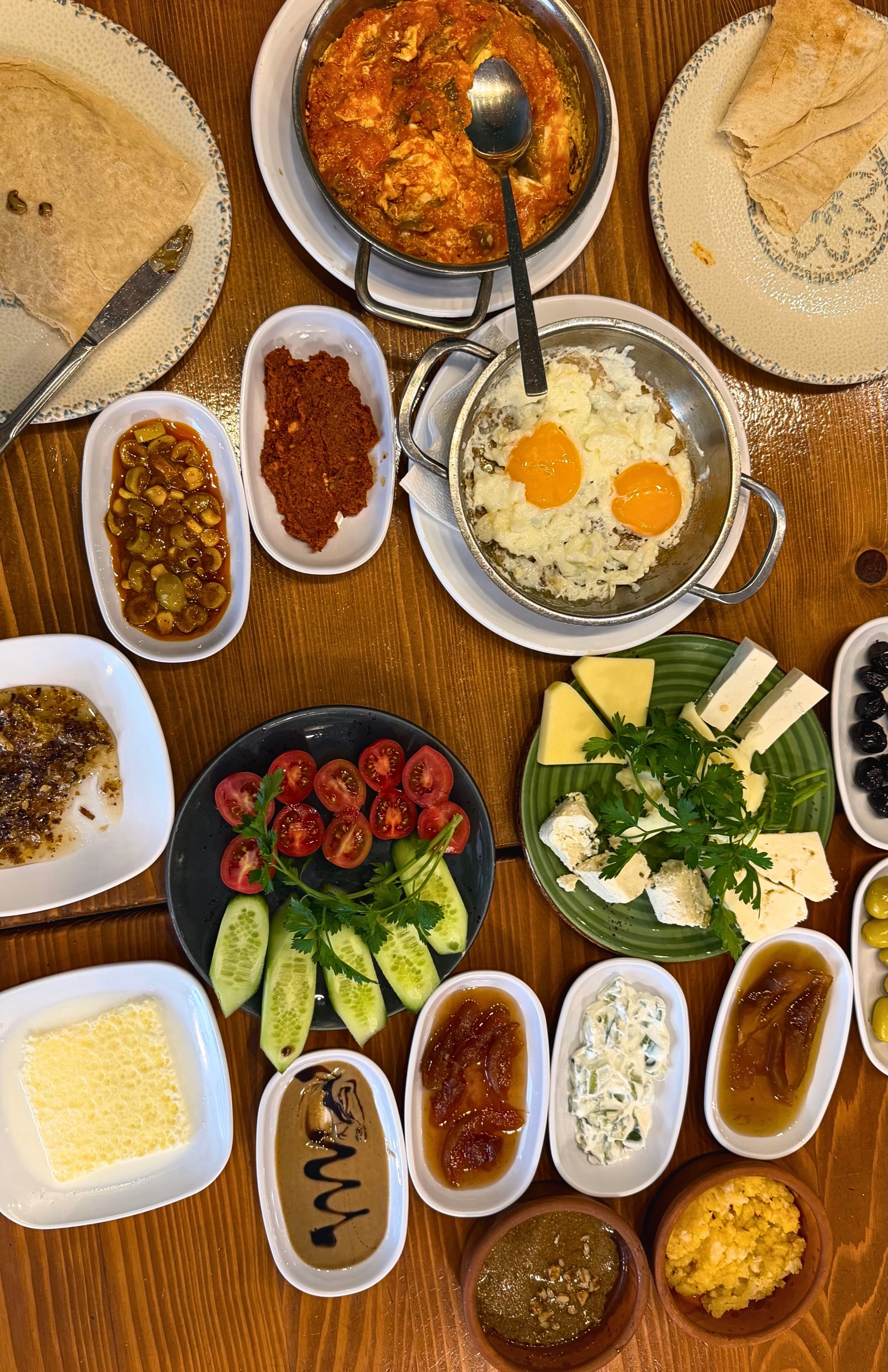 A full Turkish breakfast spread with eggs, cheese, olives, tomatoes, cucumbers, bread, honey, and small dishes.
