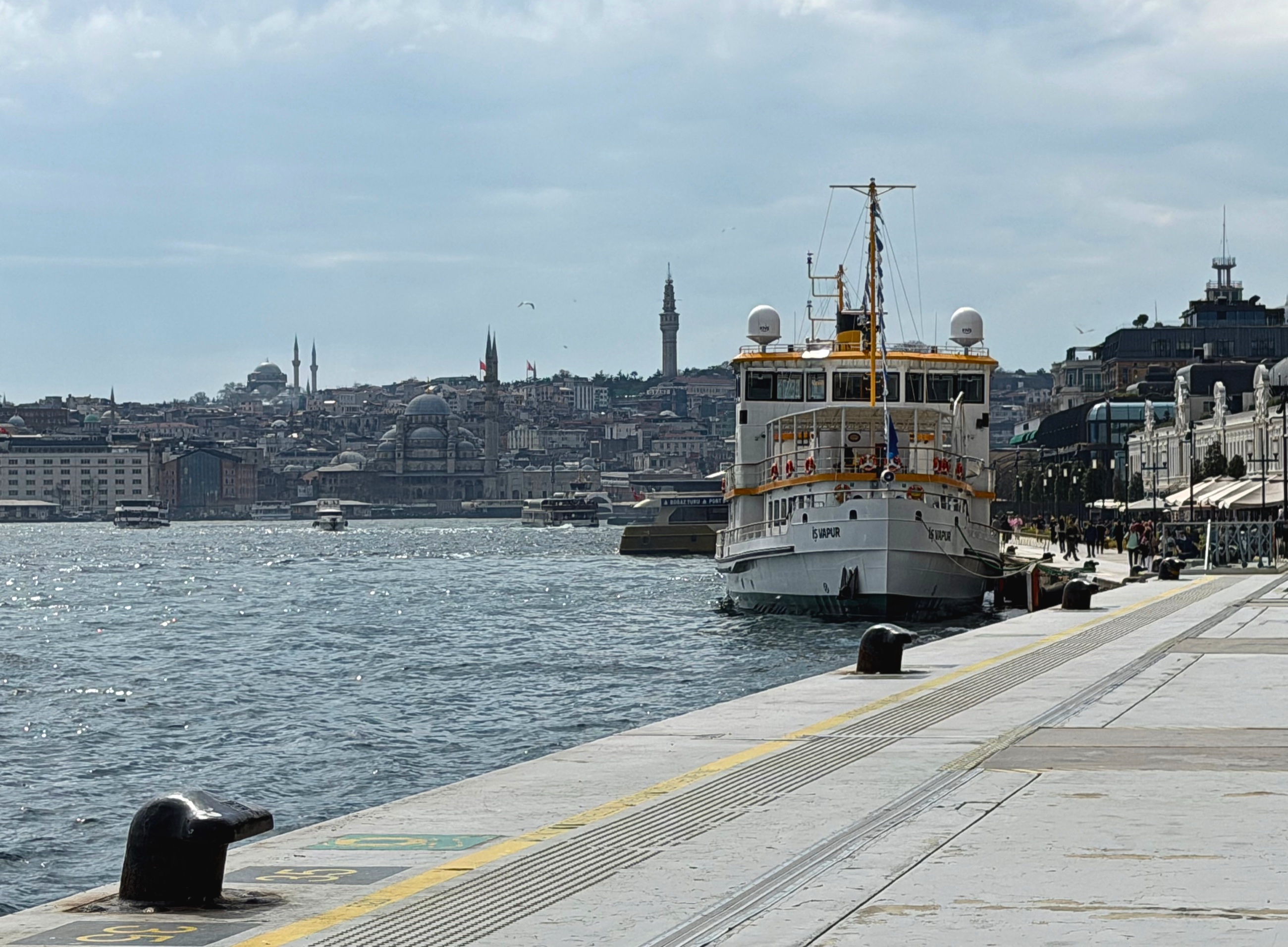 A ferry moored along the Bosphorus waterfront with Istanbul's skyline across the water.