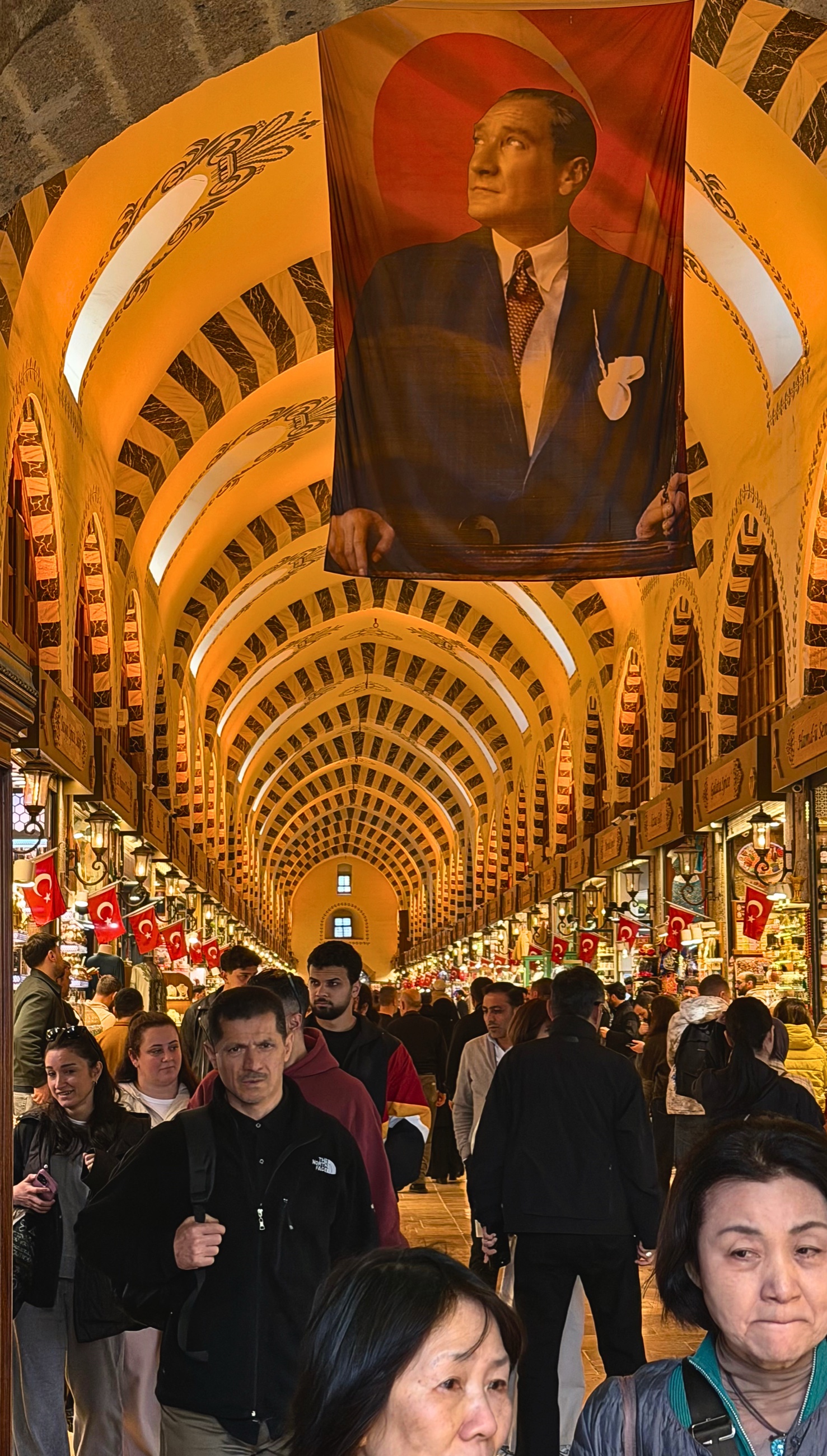 The interior of the Grand Bazaar with arched ceilings, Turkish flags, shops, and crowds.