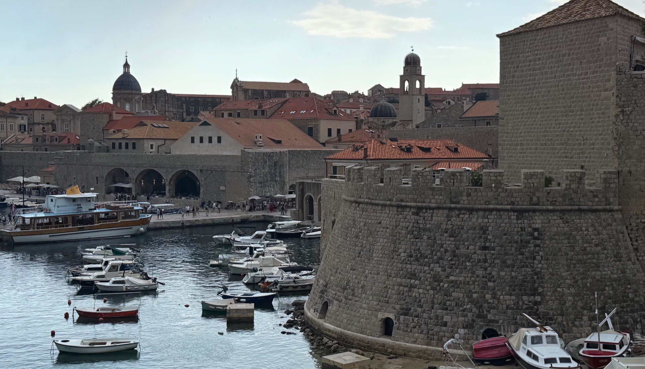 Dubrovnik's old harbor at evening, with the city walls and maritime buildings along the water.