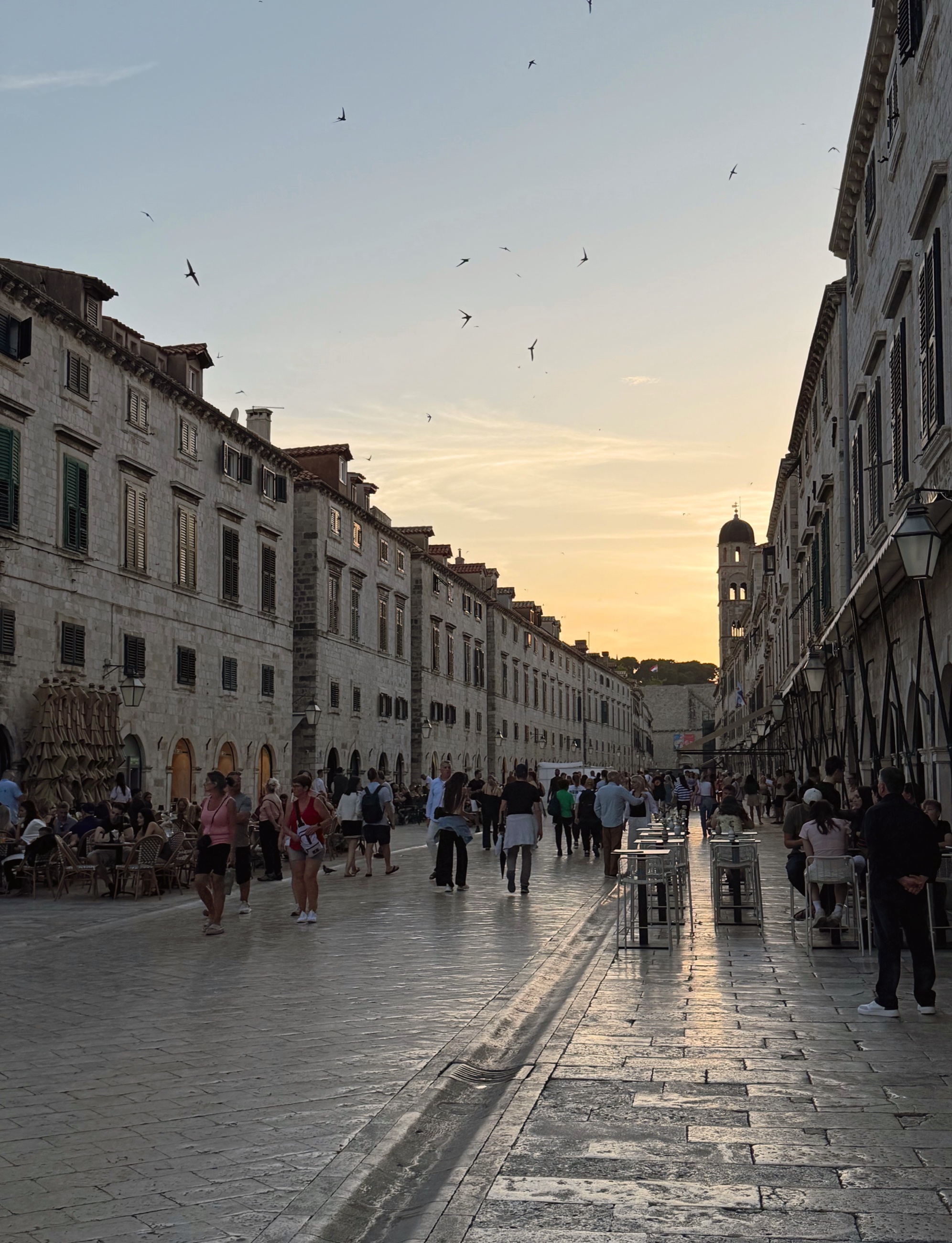 Sunset on Dubrovnik's Stradun with birds crossing the sky above the old stone street.