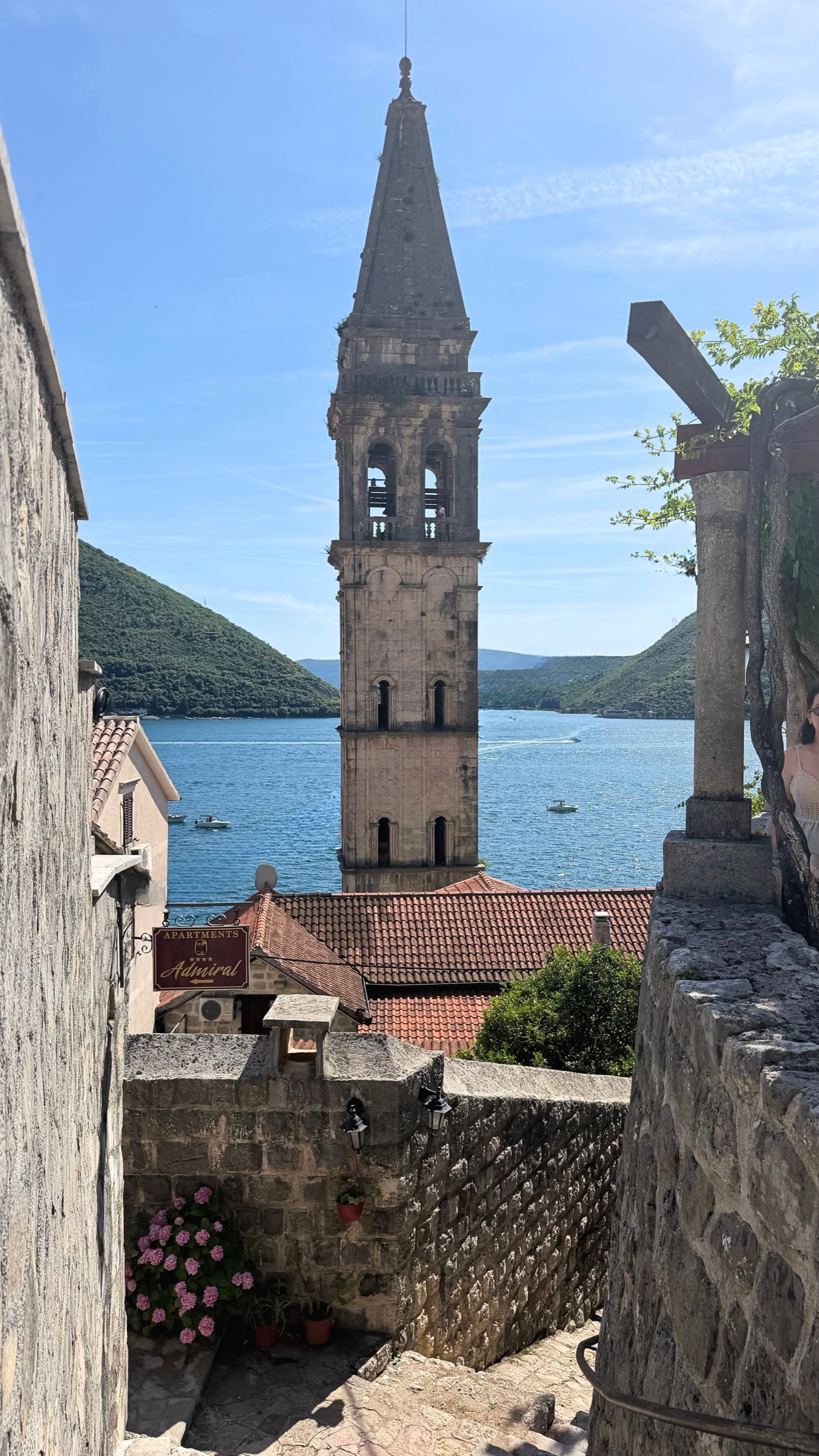 A stone stairway in Perast, with the 17th-century bell tower above the roofs and the bay beyond.