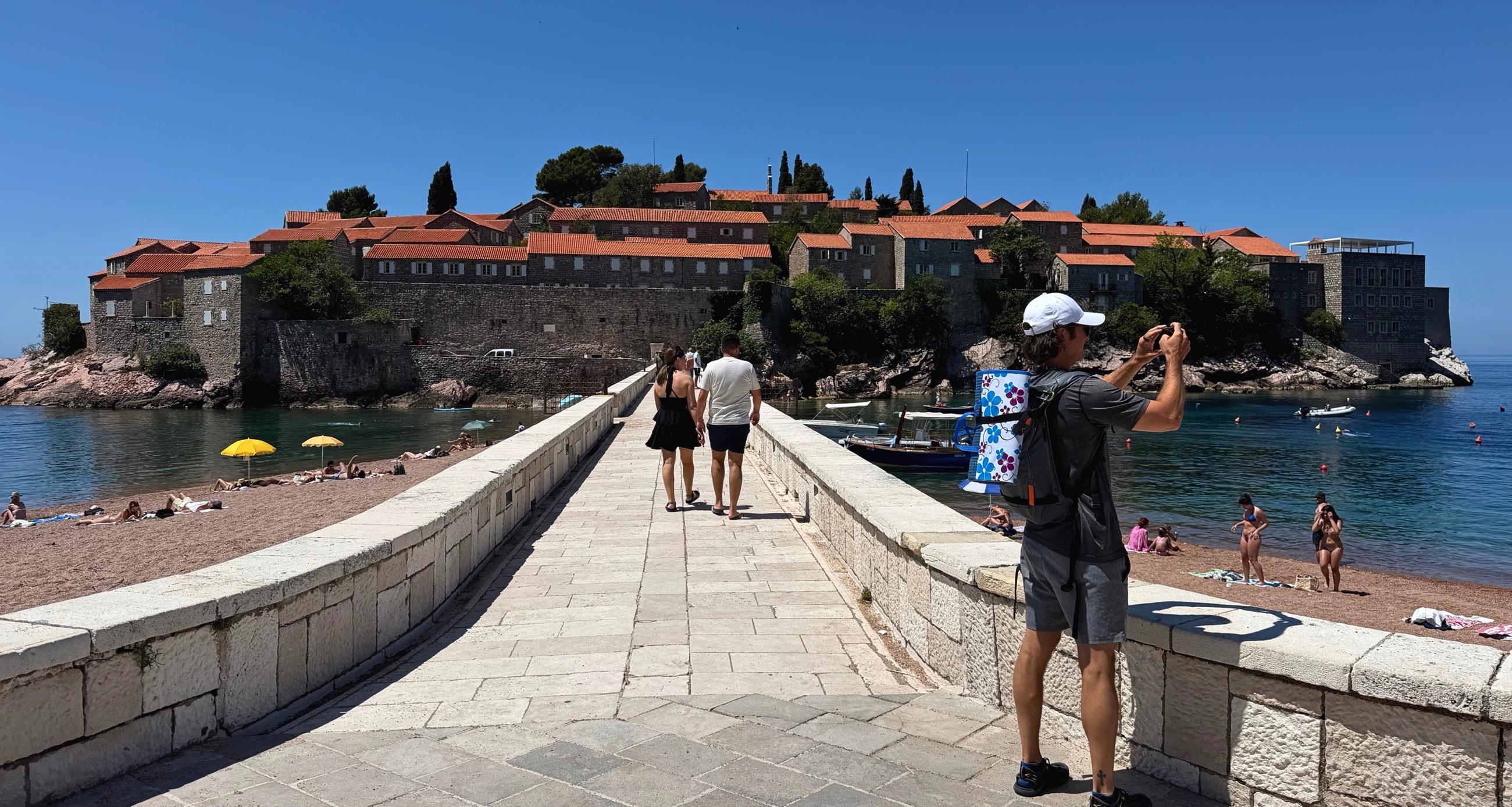 The causeway to Sveti Stefan, with beachgoers and the fortified island ahead.