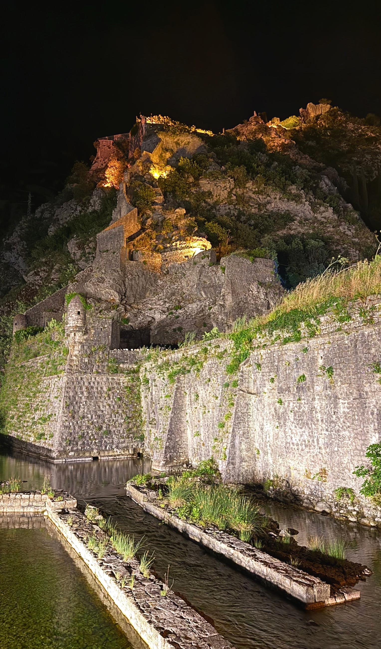 Kotor’s medieval fortifications lit after dark, climbing from the old city into the mountain above.