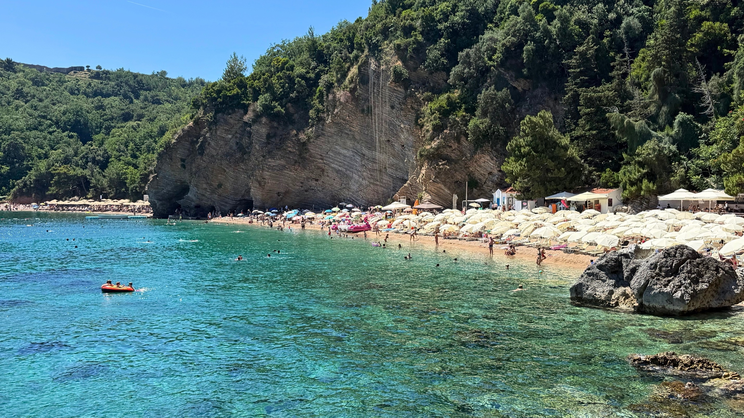Mogren Beach, with clear water, limestone cliffs, and a busy summer shoreline along the coast