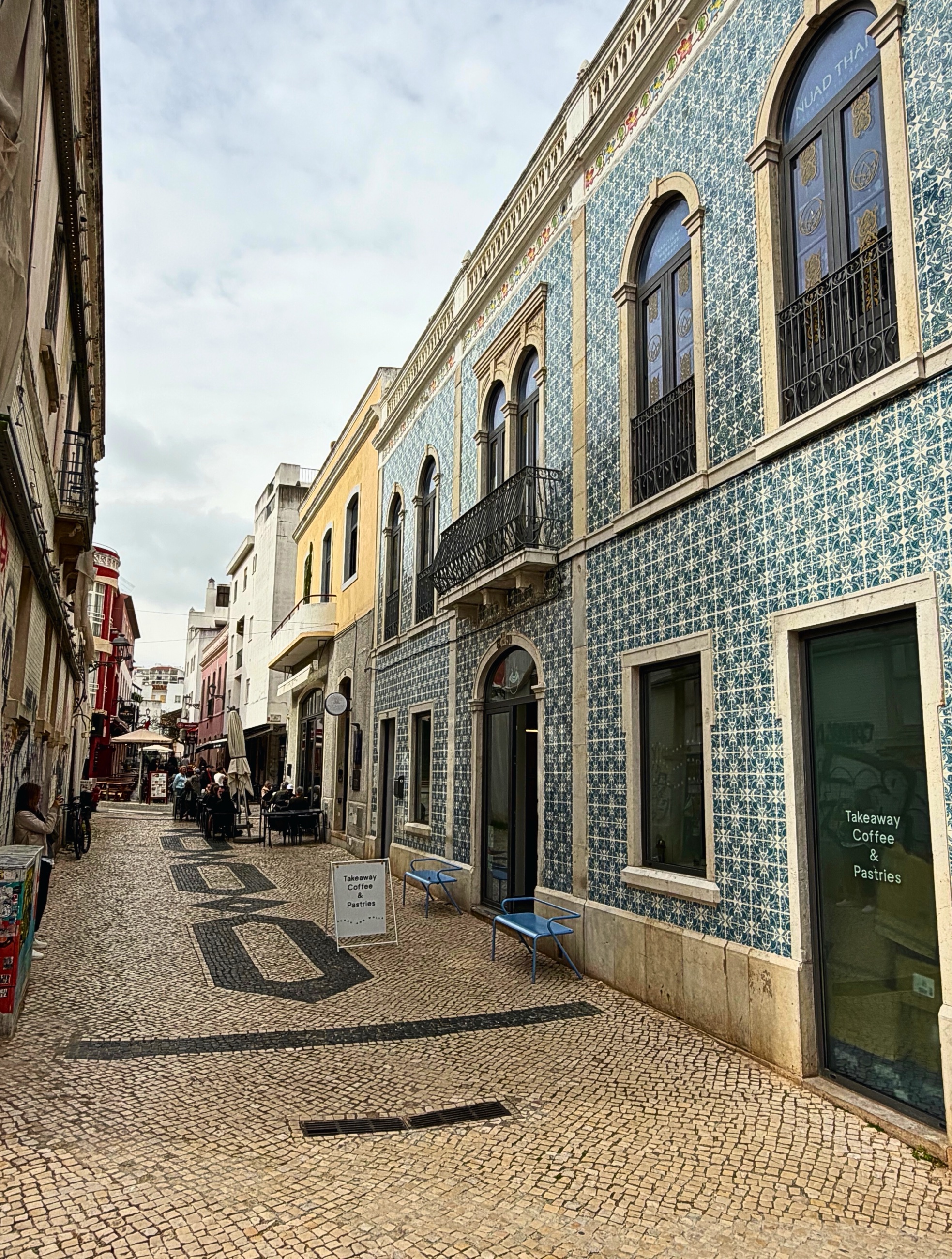 A tiled building and patterned calçada pavement on a narrow street in Lagos.