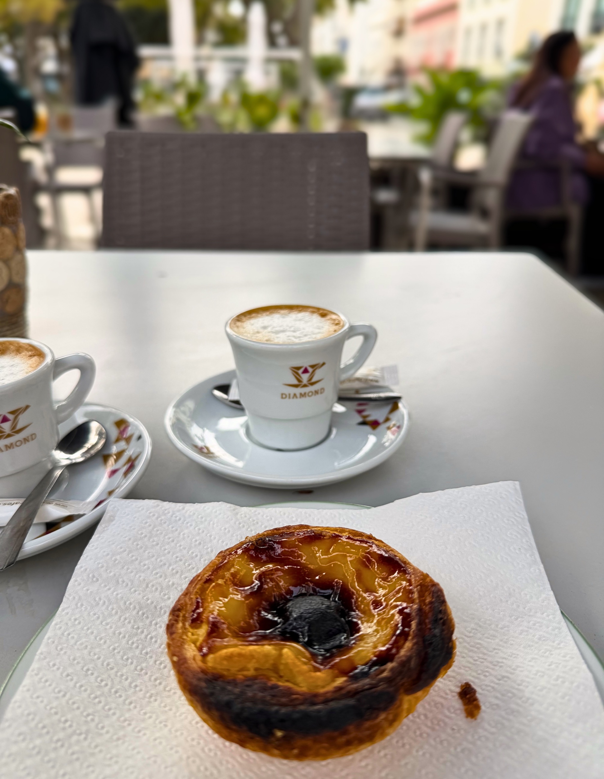 A pastel de nata and cups of coffee on an outdoor café table.