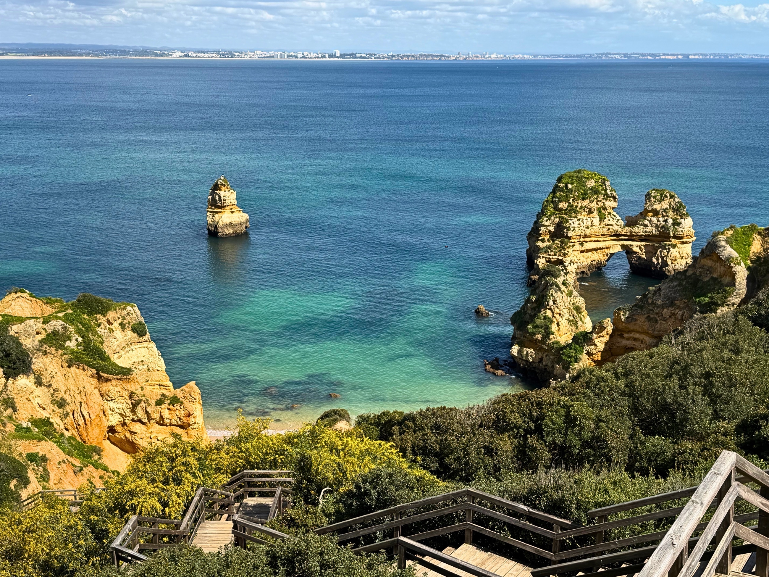 Wooden stairs descending toward blue water and rock formations near Ponta da Piedade.