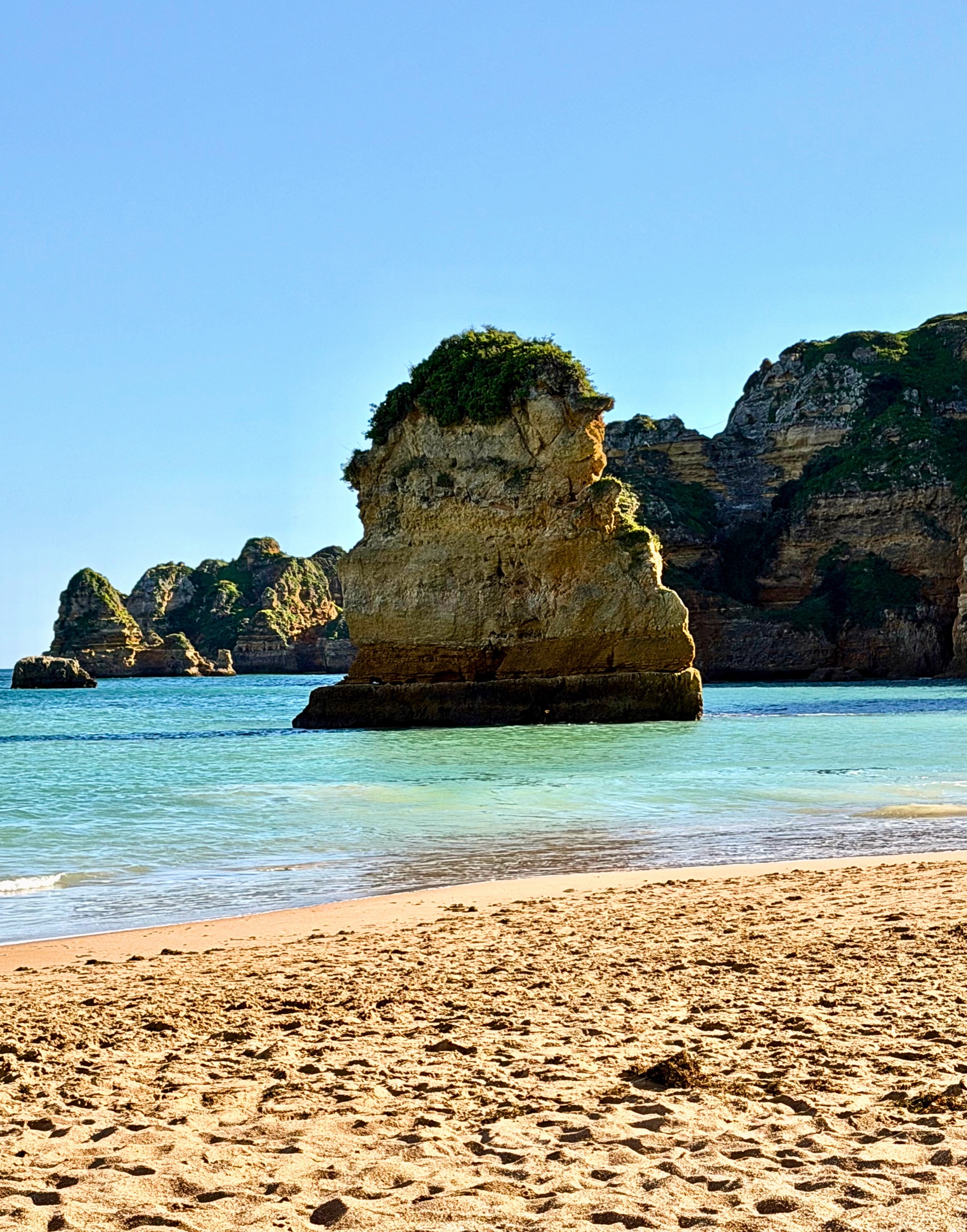 A beach-level view of sand, sea, and rock formations along the Algarve coast.