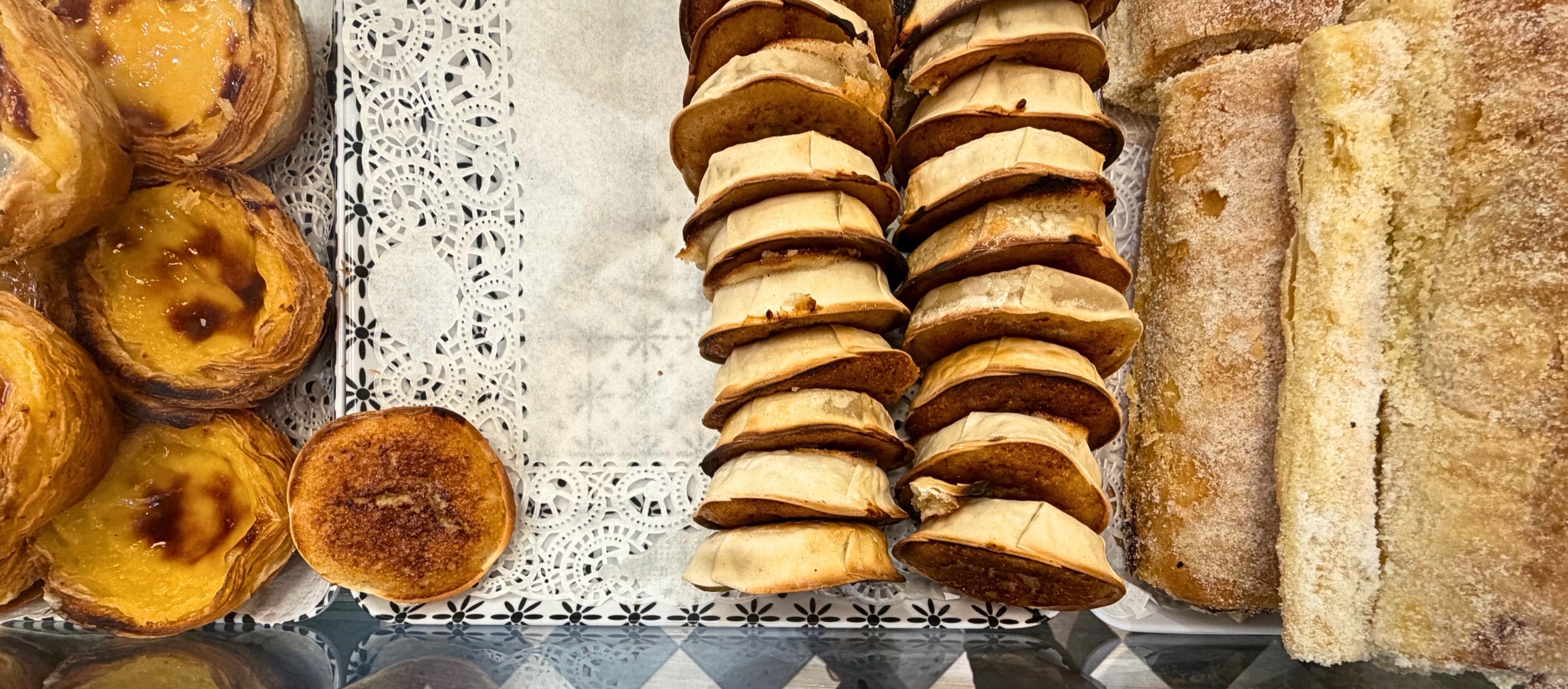 A bakery case in Sintra filled with pastéis de nata, queijadas, and travesseiros.