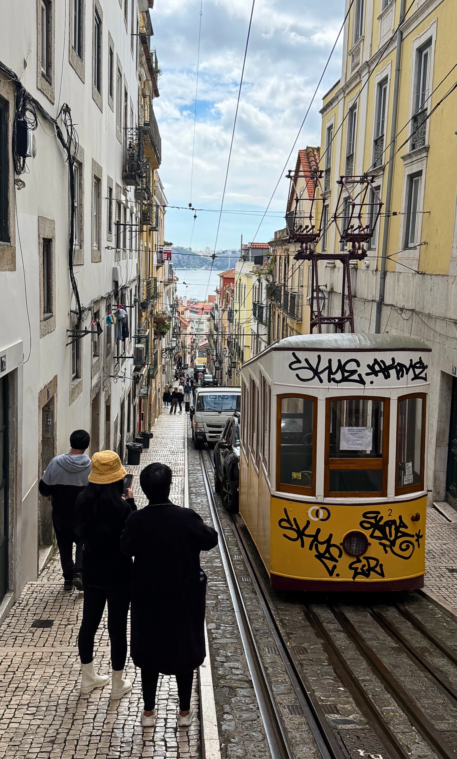 A yellow tram moving through Lisbon streets.