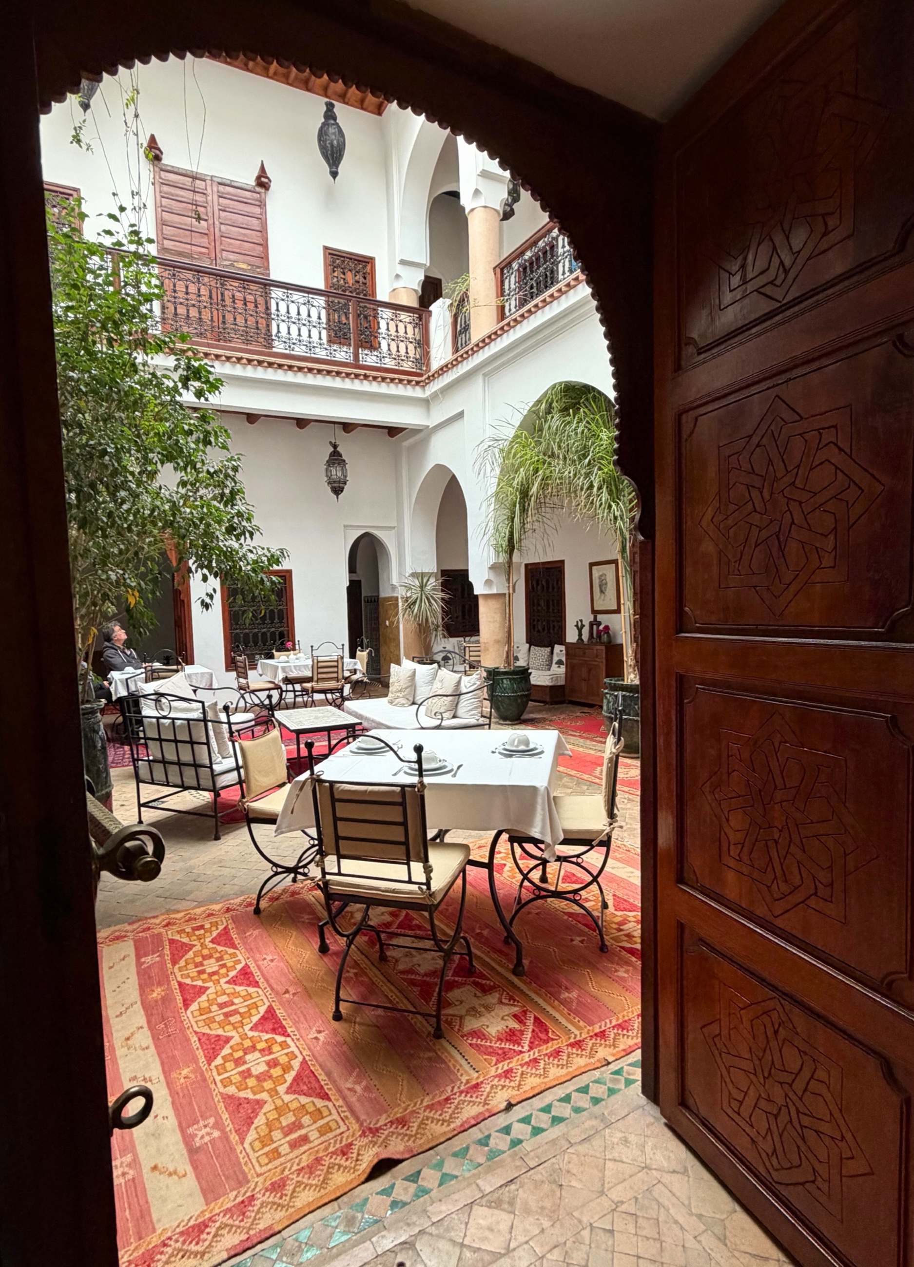 An interior courtyard in a Marrakesh riad with tilework, arches, plants, and a central fountain.