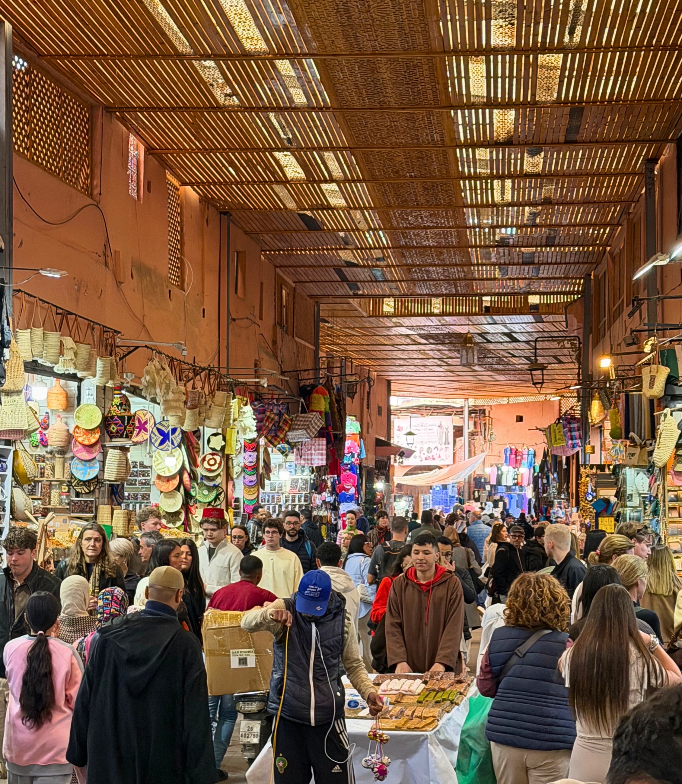 A busy covered souk aisle in Marrakesh with shops and people moving through the passage.