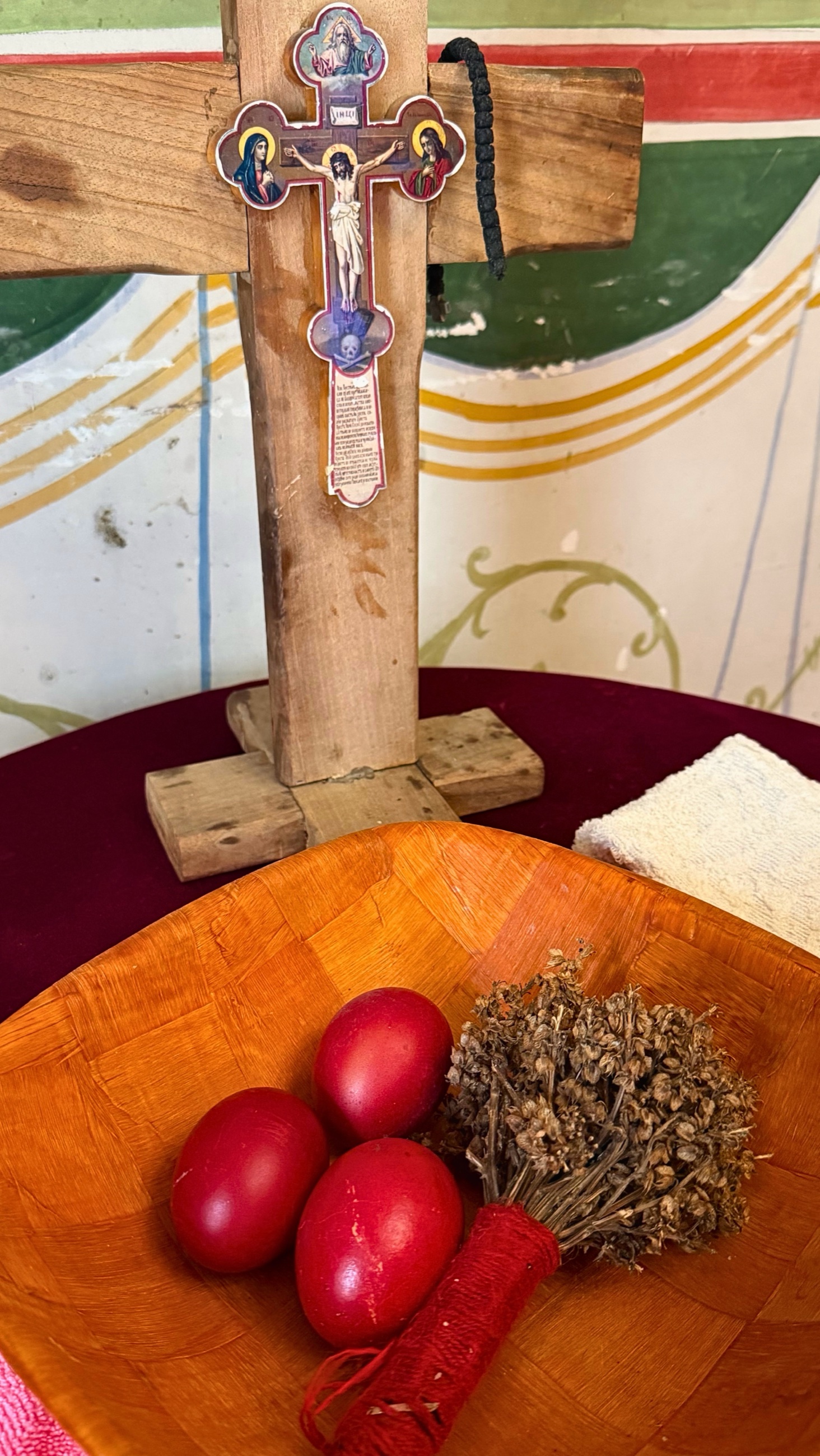 Red Easter eggs in a wooden bowl beneath a wooden cross.