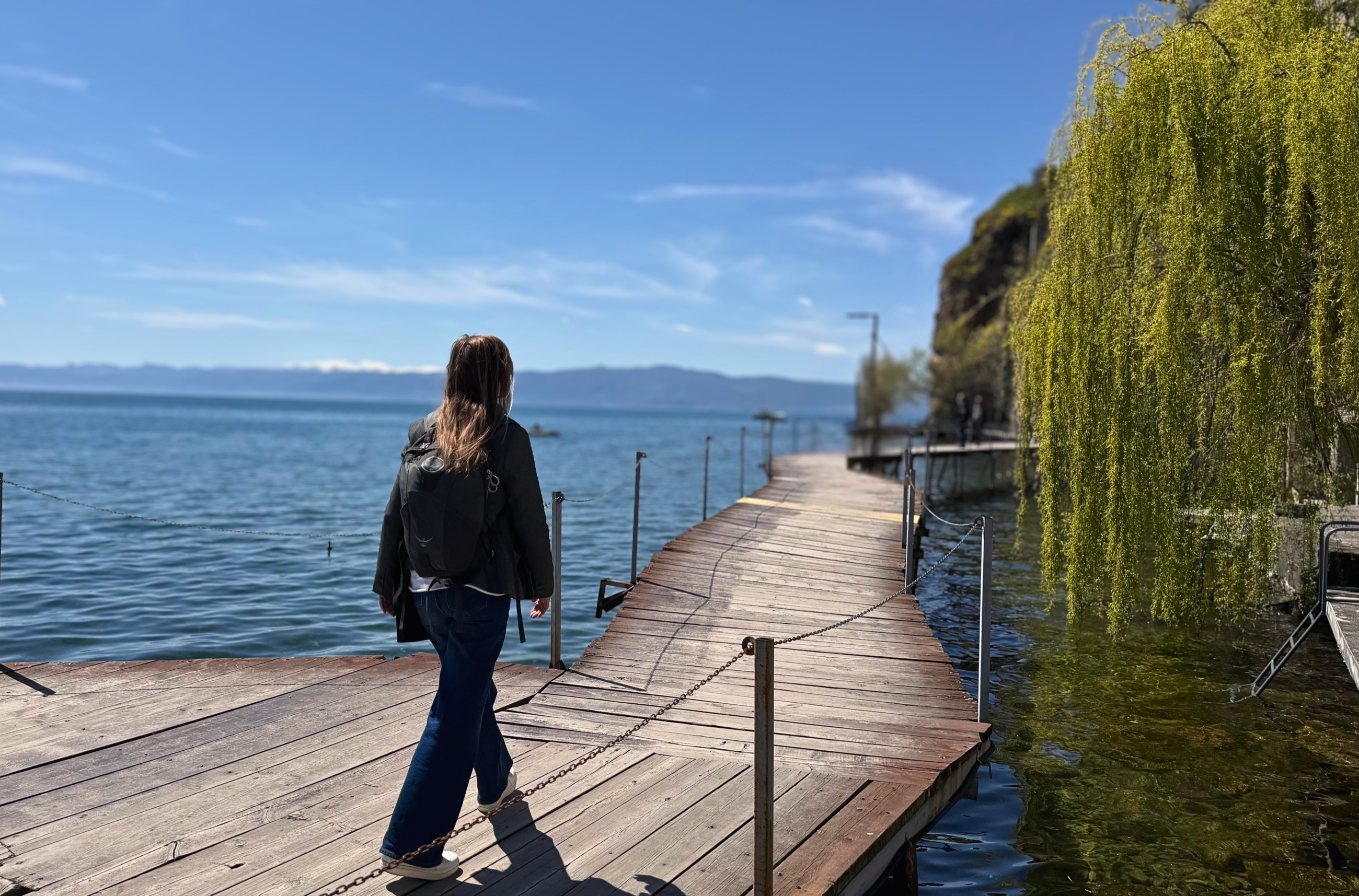 Stephanie walking along a wooden boardwalk beside Lake Ohrid.