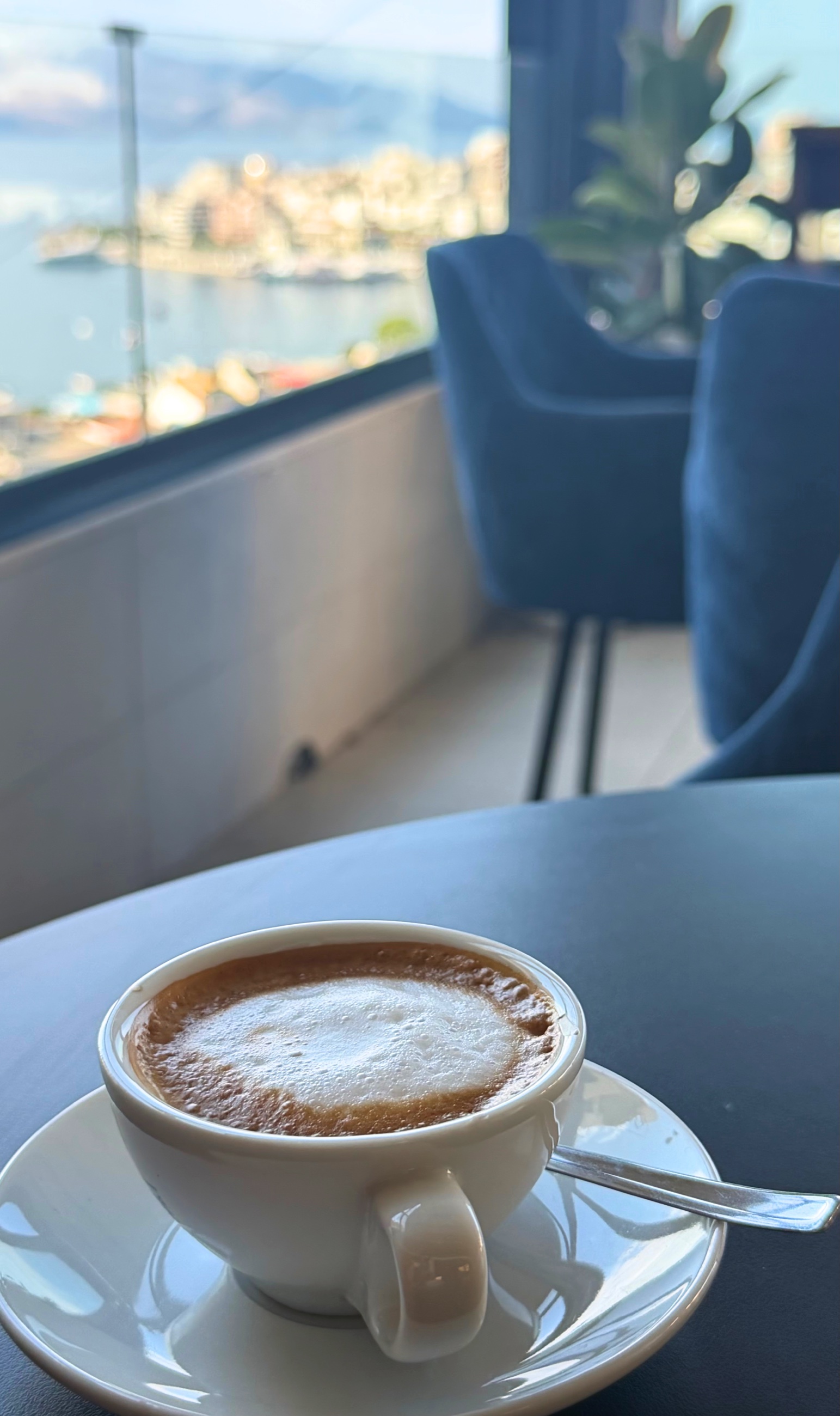 An espresso macchiato on a café table with Sarandë and the Ionian bay softly blurred in the background.