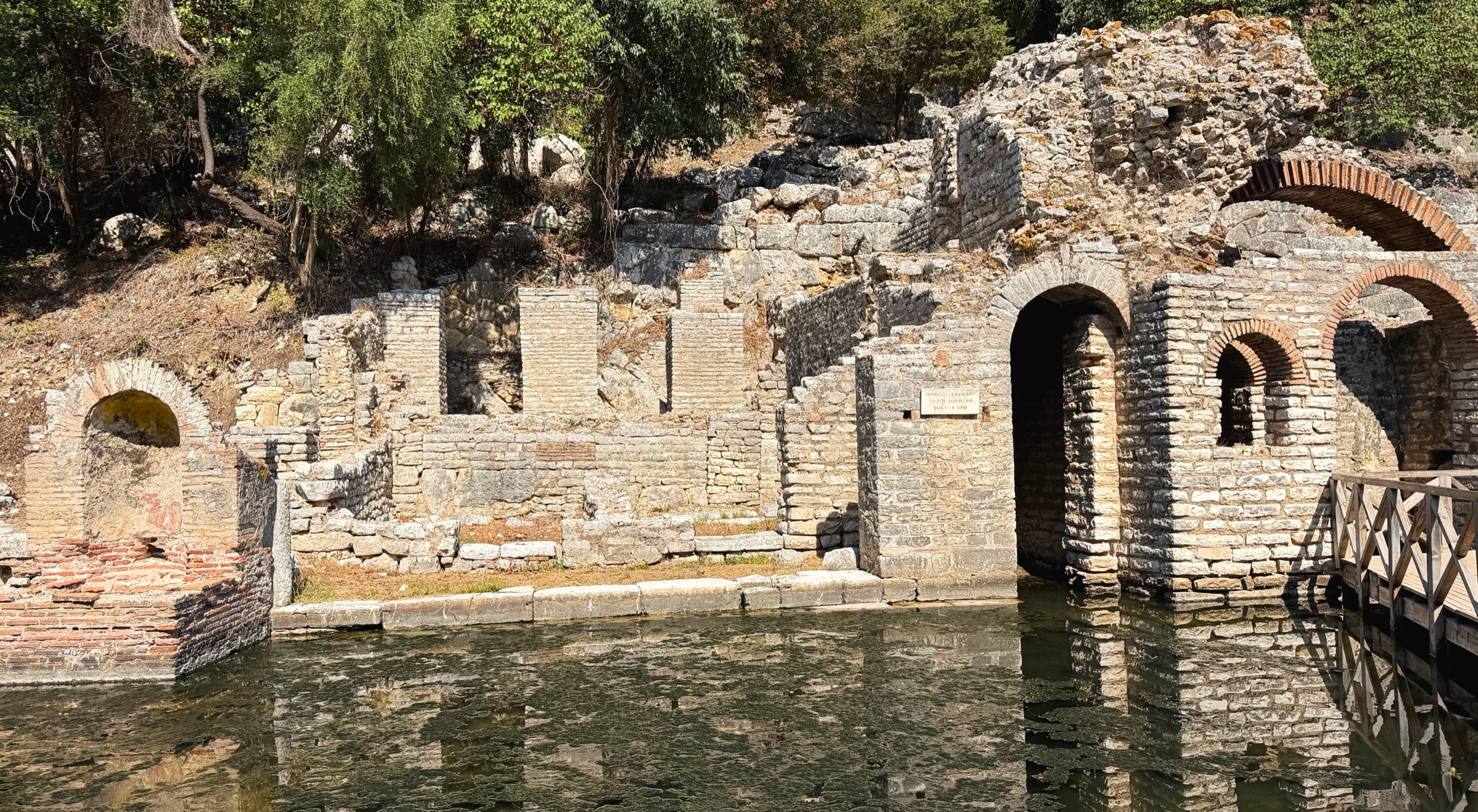 Stone and brick remains of Butrint's Roman baths beside standing water.