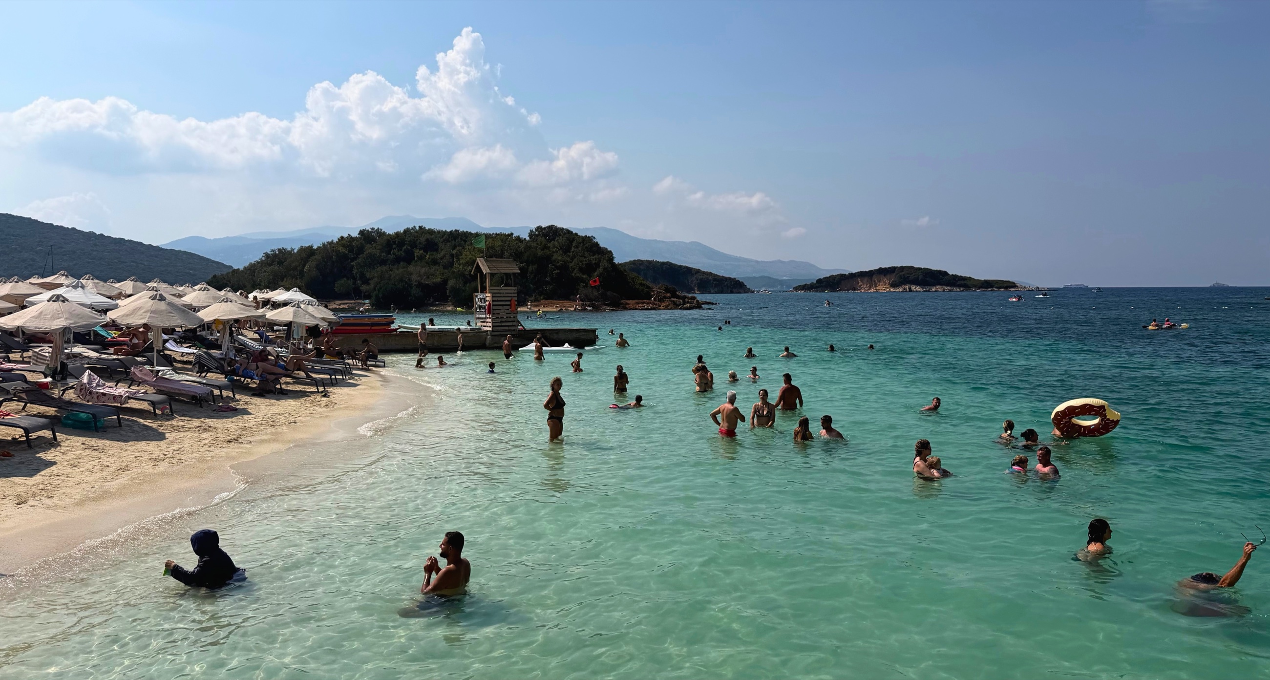 Swimmers in clear turquoise water along a beach in Ksamil.