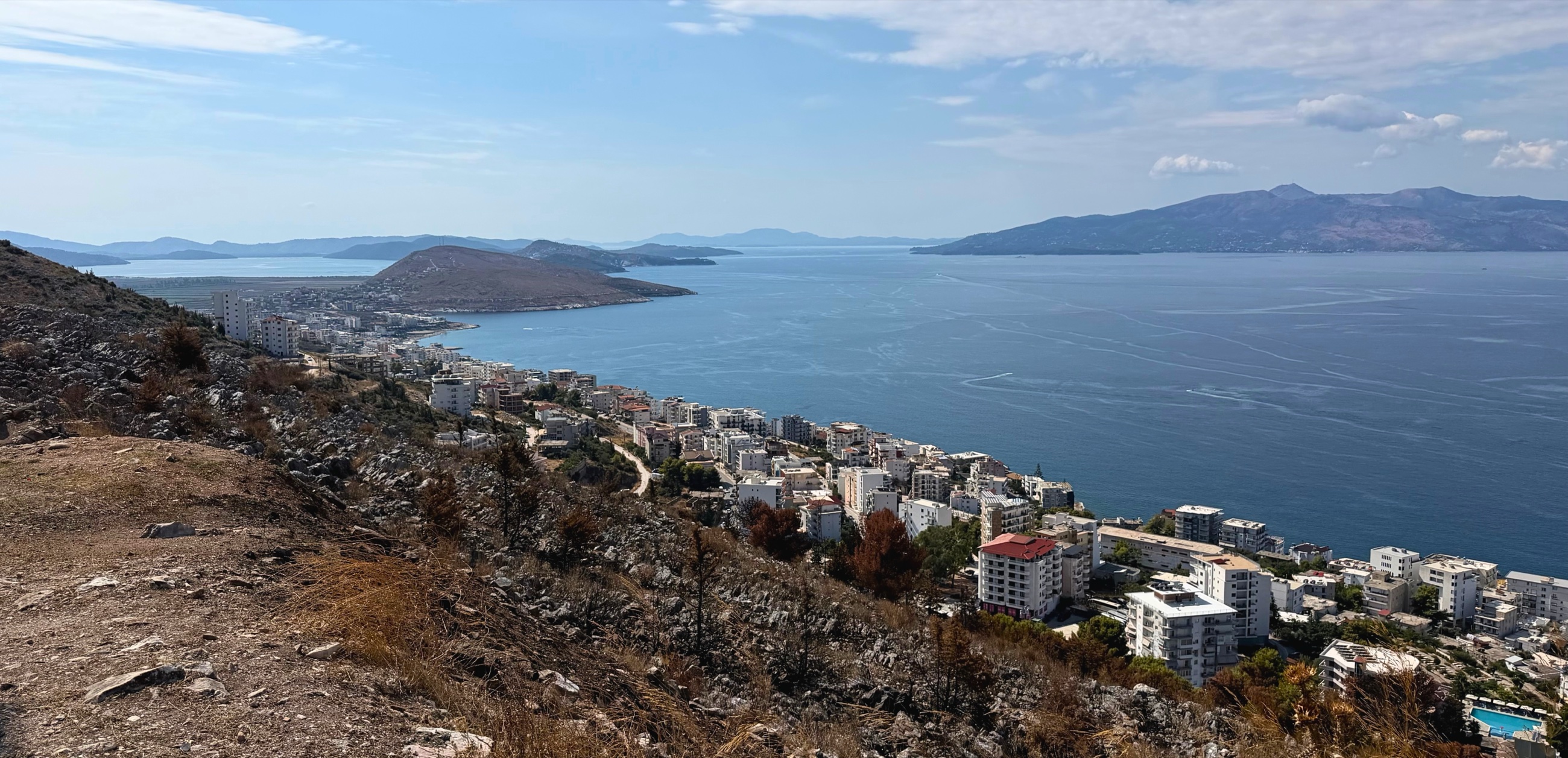 View south from the hills above Sarandë across the city, Ionian Sea, and coastline toward the Butrint landscape.
