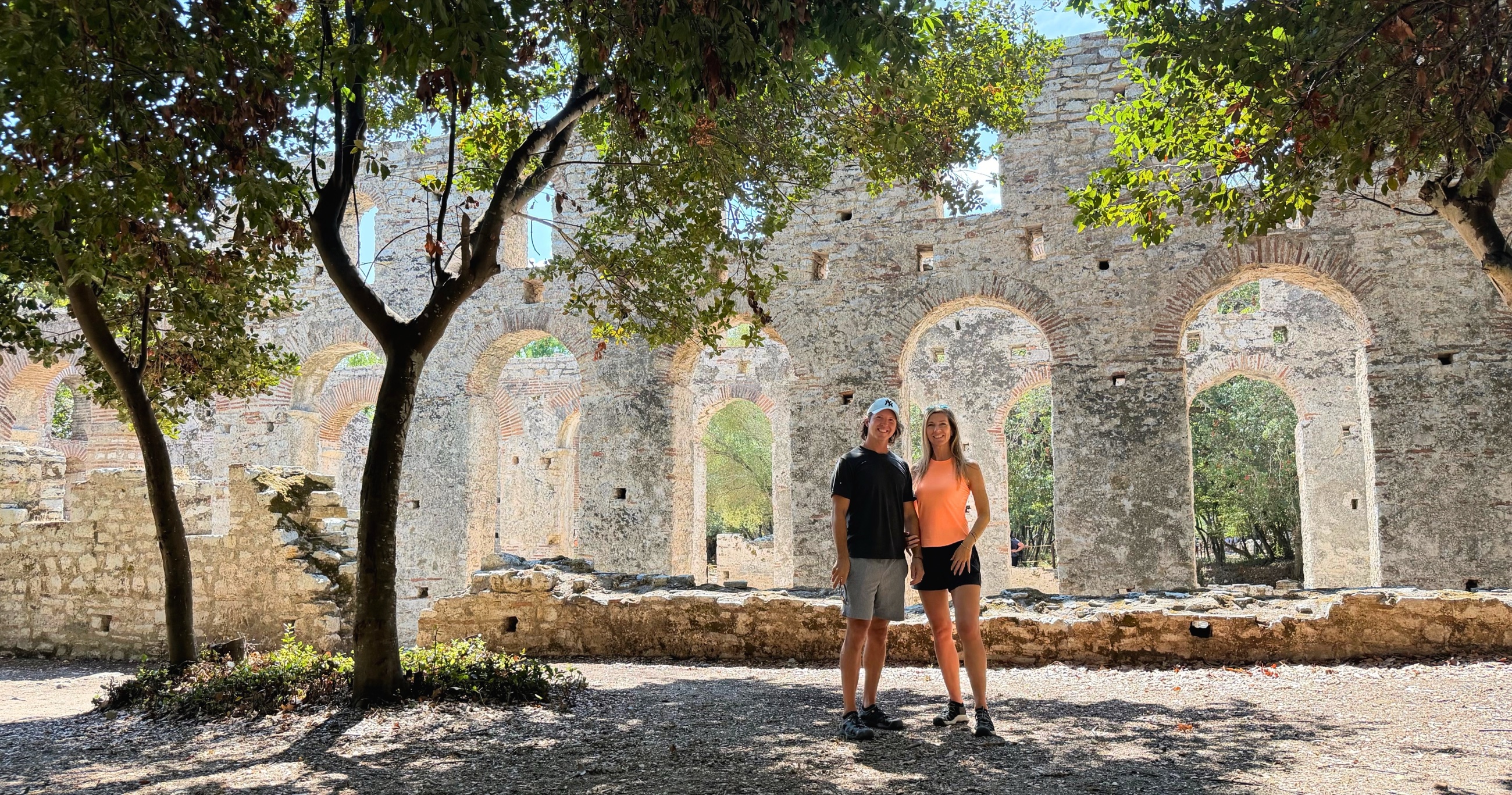 Sam and Stephanie standing beneath the arches and trees of Butrint's Great Basilica.
