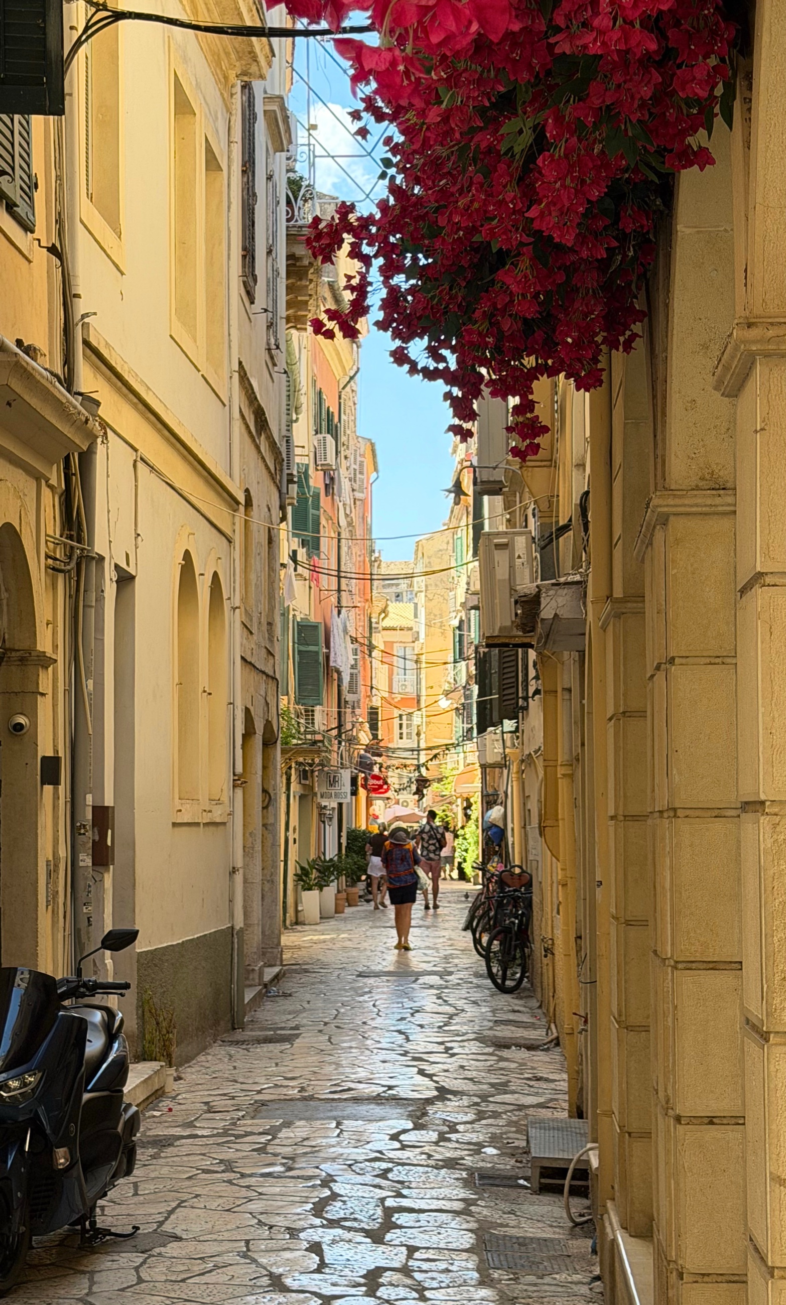 A narrow stone lane in Corfu Old Town beneath bright bougainvillea and shuttered buildings.