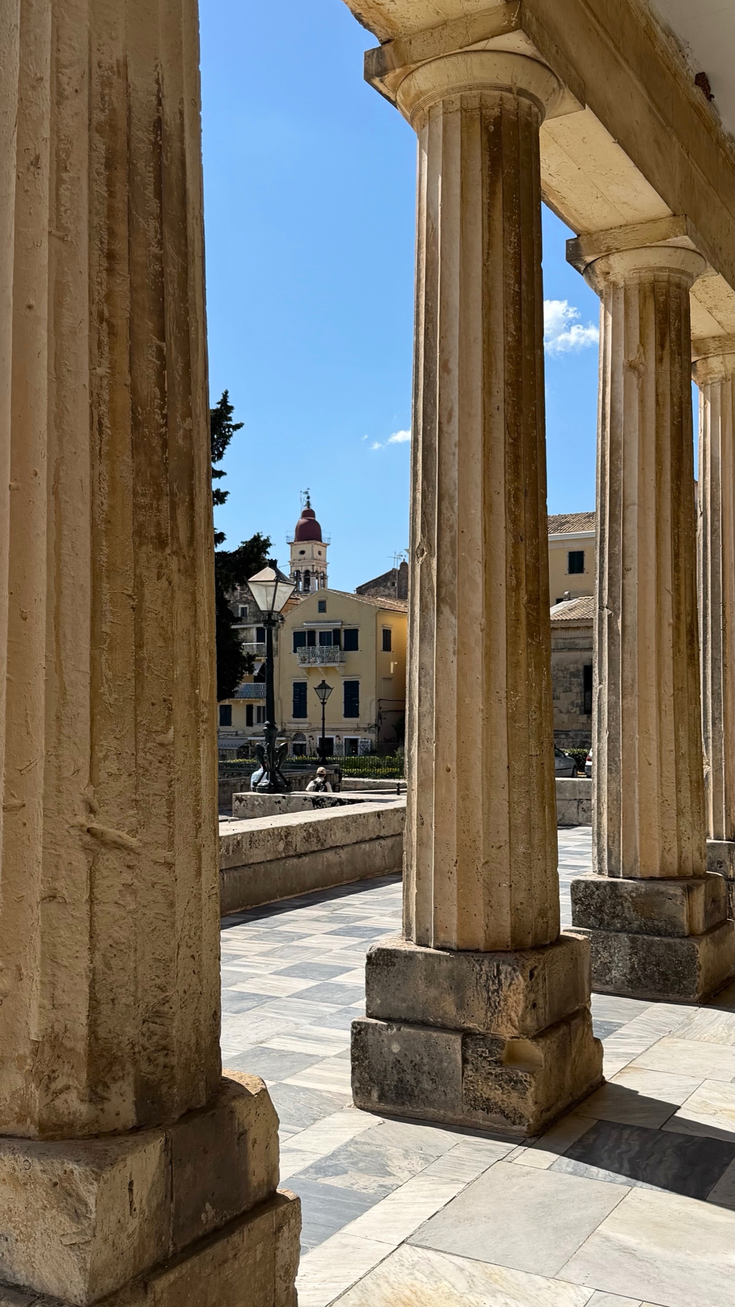 Stone columns at the Palace of St. Michael and St. George framing a Corfu bell tower.