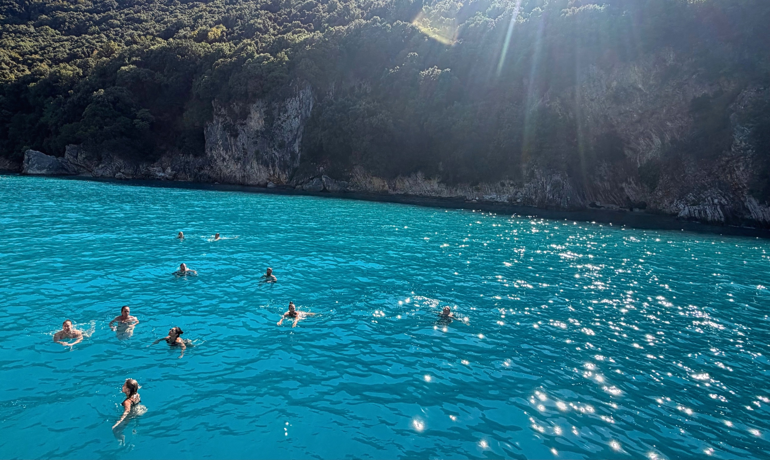 Swimmers in turquoise water below the shaded cliffs at Kakome.