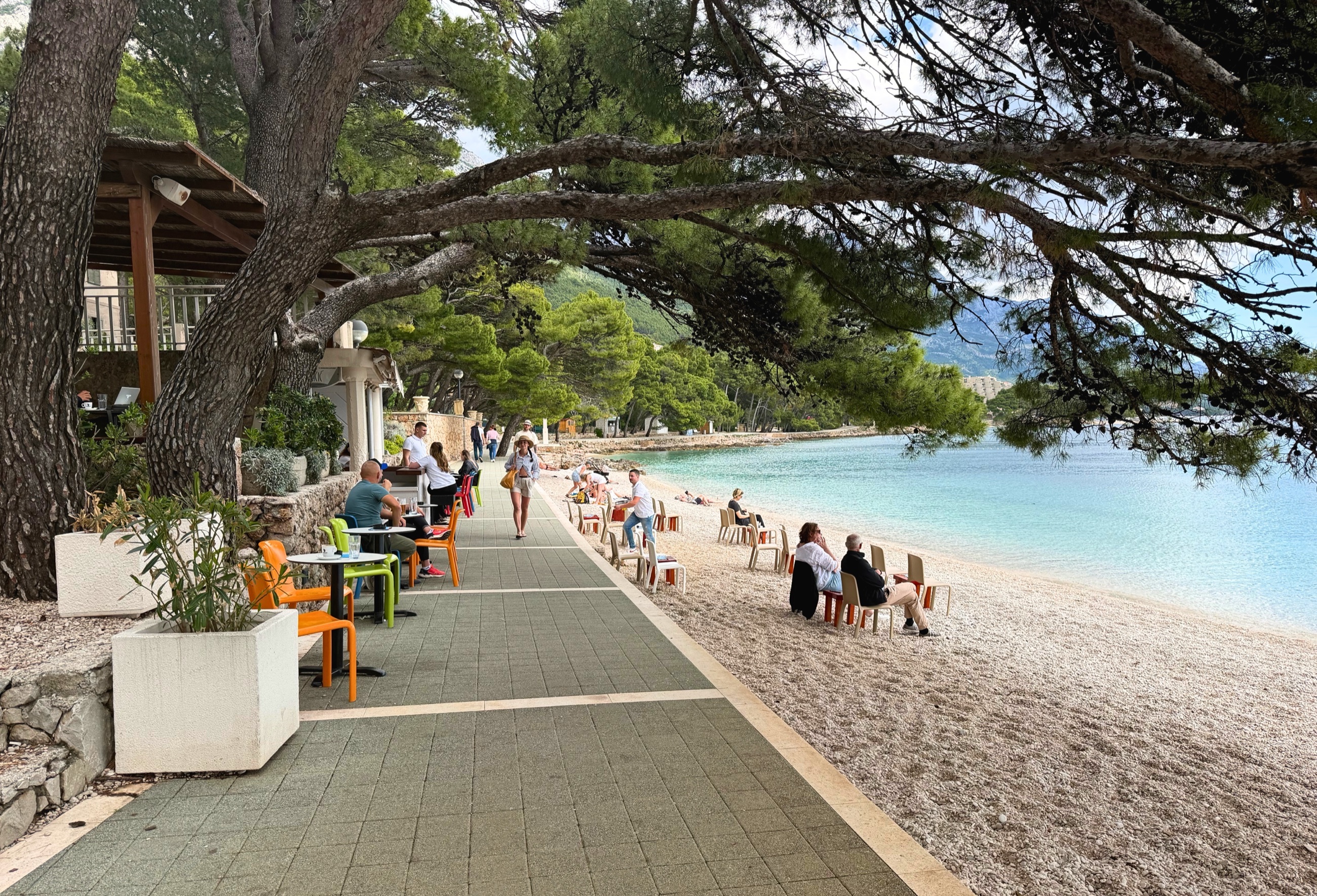 Brela coastal path with pine shade and café tables near the water