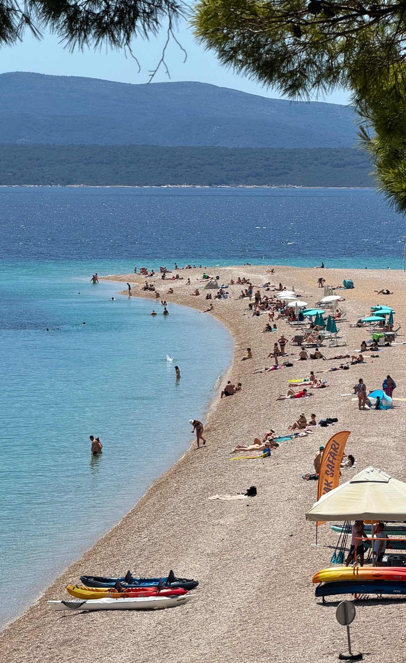 Zlatni Rat beach at beach level with pebbles, clear water, and the curved shoreline