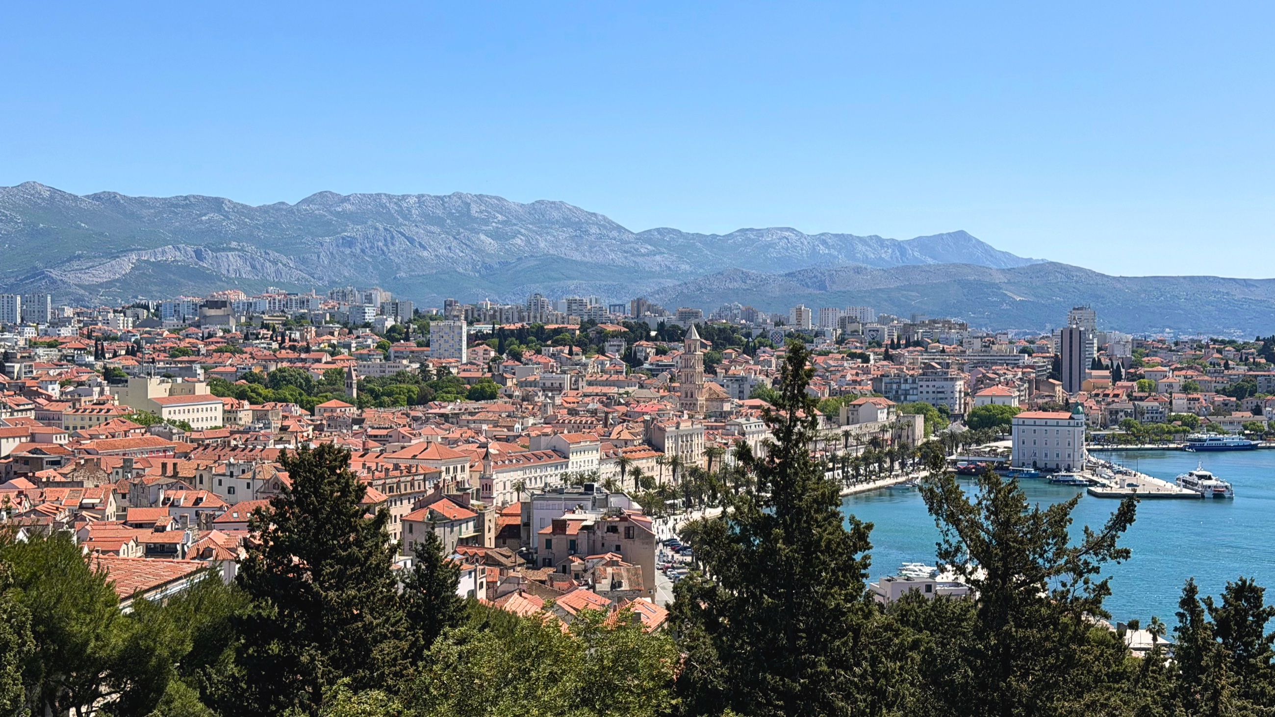 View of Split from Marjan Hill, with red rooftops, the Adriatic Sea, mountains, and the old city below.