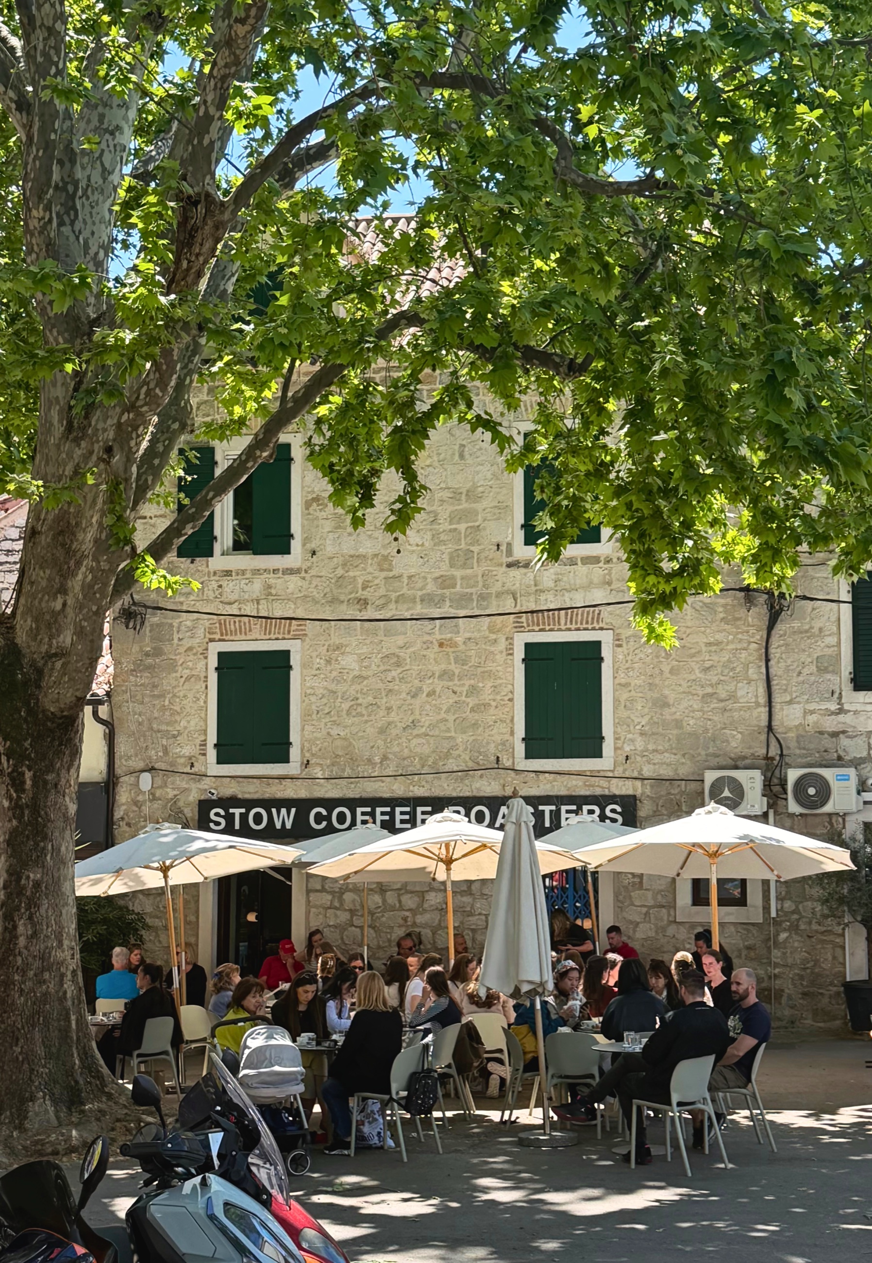 Outdoor seating at Stow Coffee Roasters in Split, with tables set beneath shade near the neighborhood street.