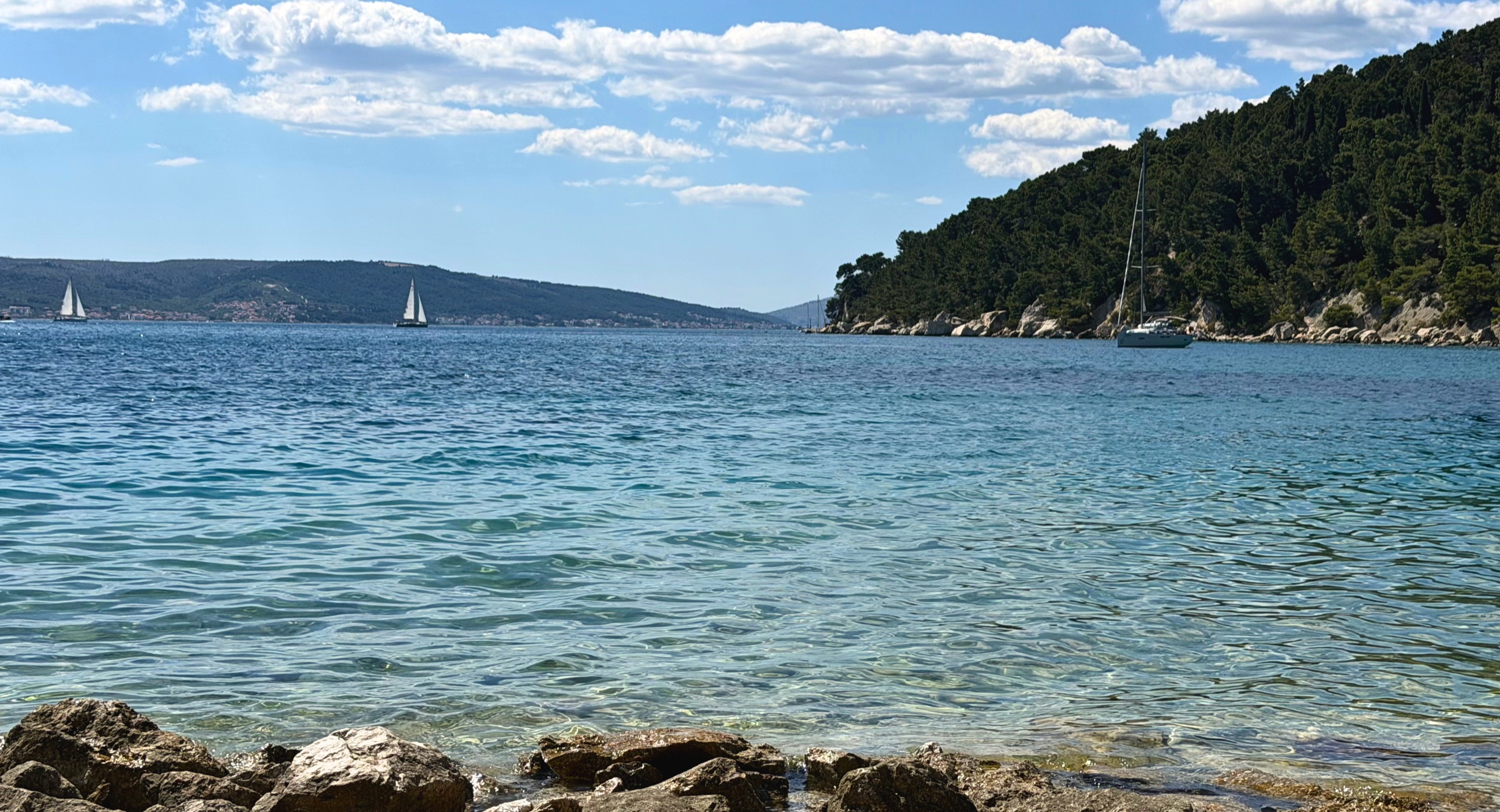 Kašjuni Beach in Split, with clear Adriatic water, stone shore, and Marjan Hill behind it.