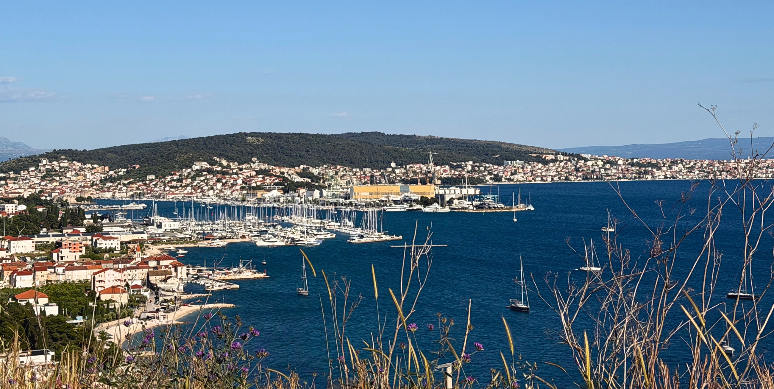 Coast near Trogir, with red roofs, marina boats, and open Adriatic water.