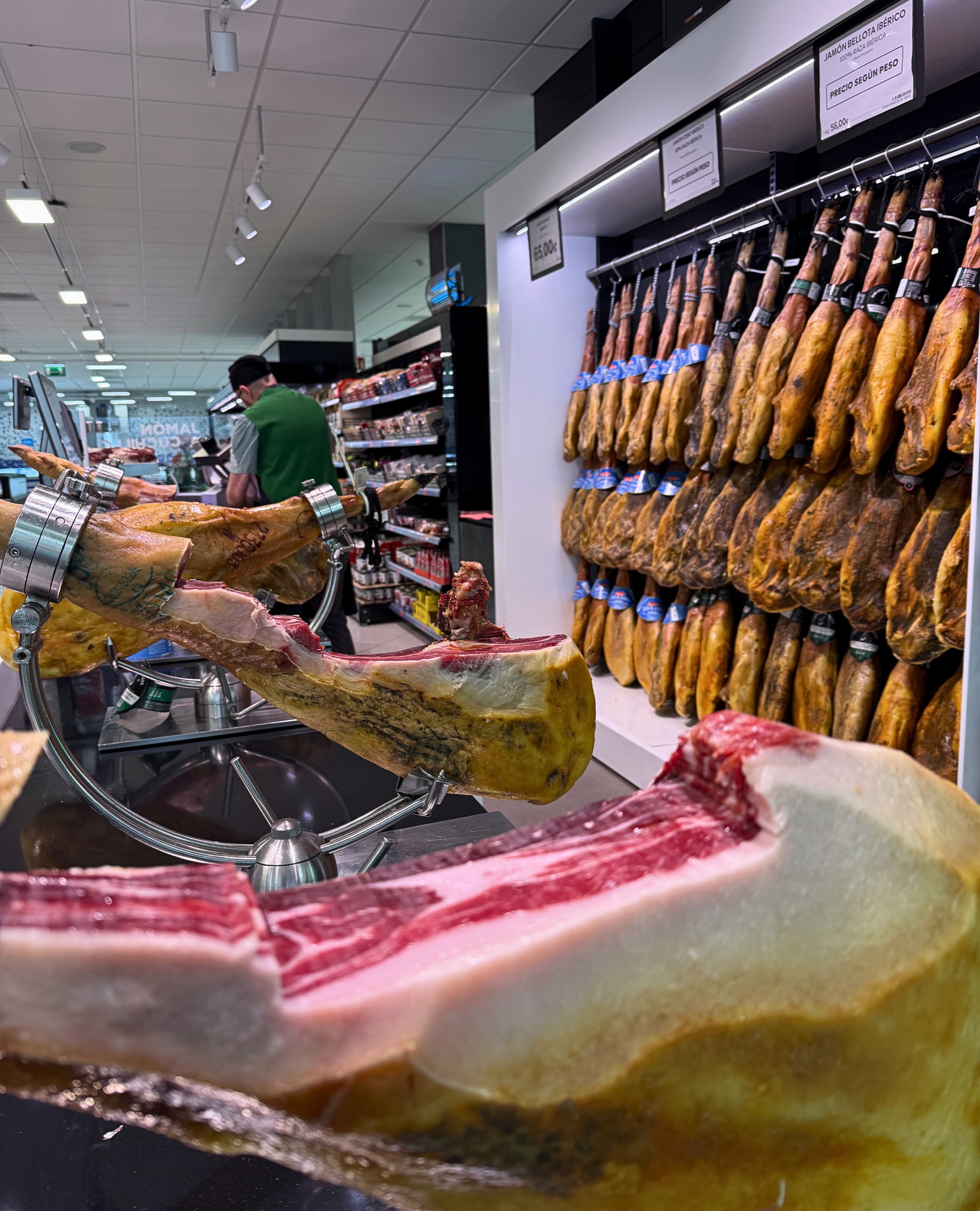Jamón at a meat counter in Tenerife with cured hams hanging in the background.