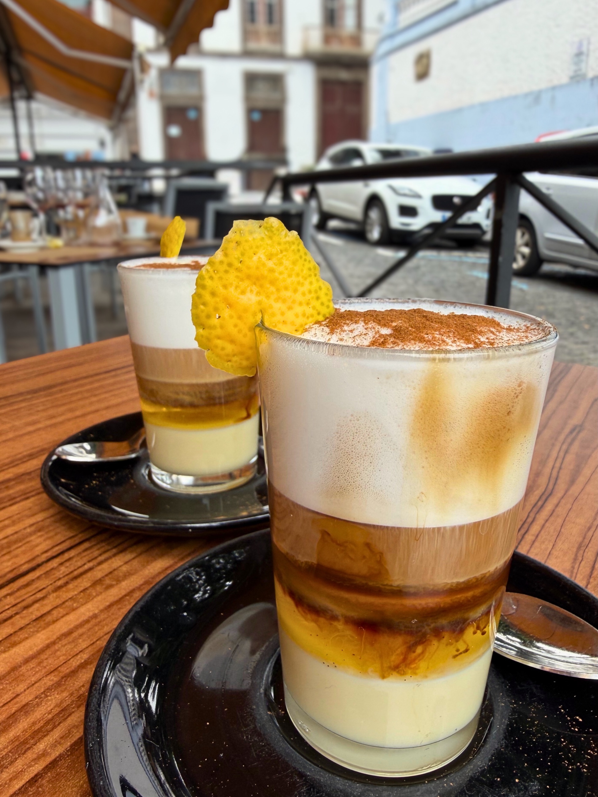 Two barraquito coffees with layered milk, coffee, foam, and lemon peel.