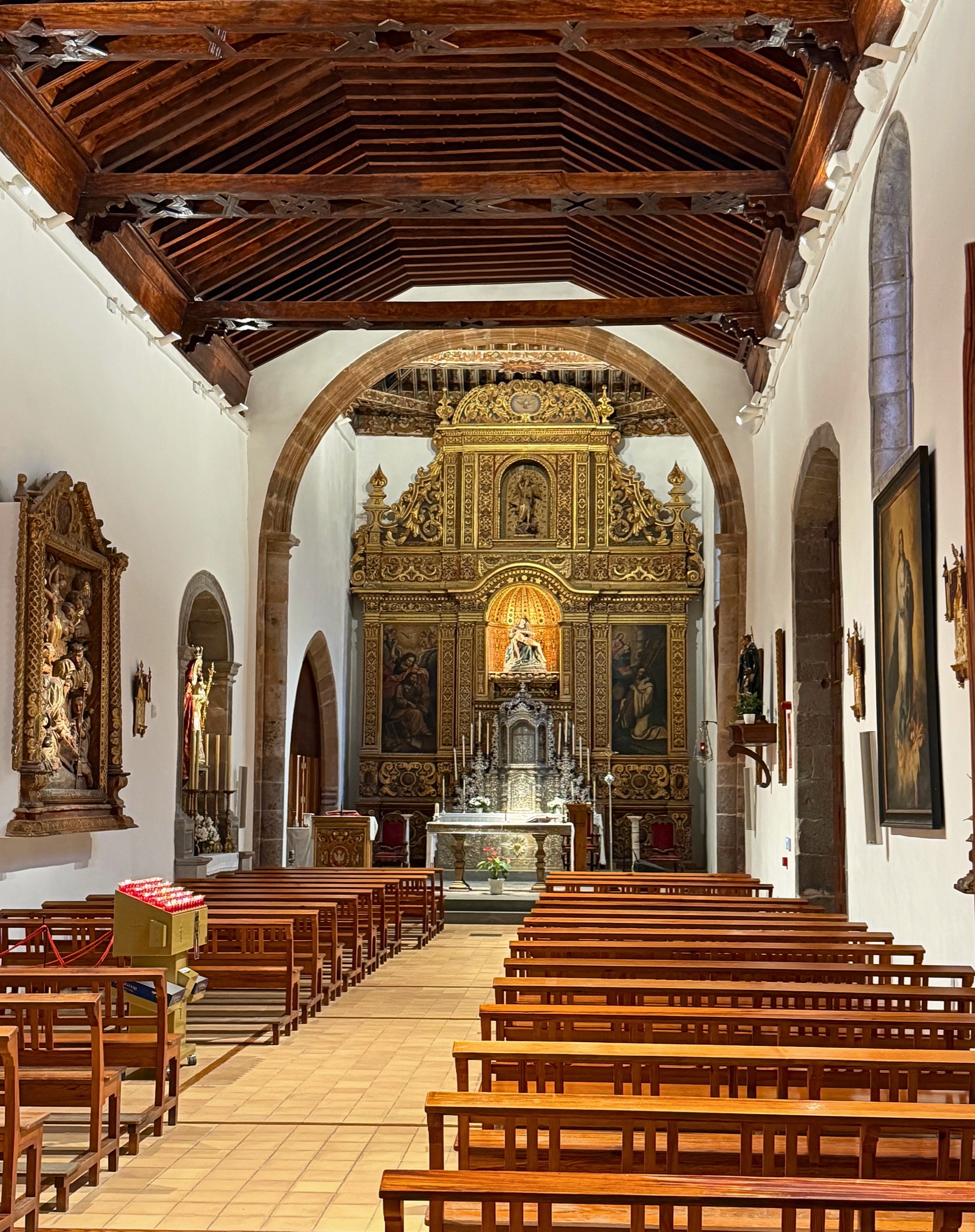 Interior of a small La Laguna church with wooden pews, a timber ceiling, and a gold altarpiece.