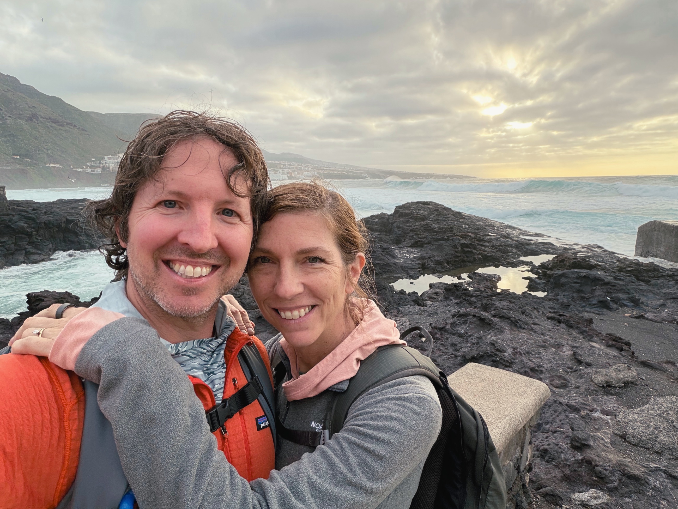Sam and Stephanie smile for a selfie beside Tenerife’s rocky coast near sunset.