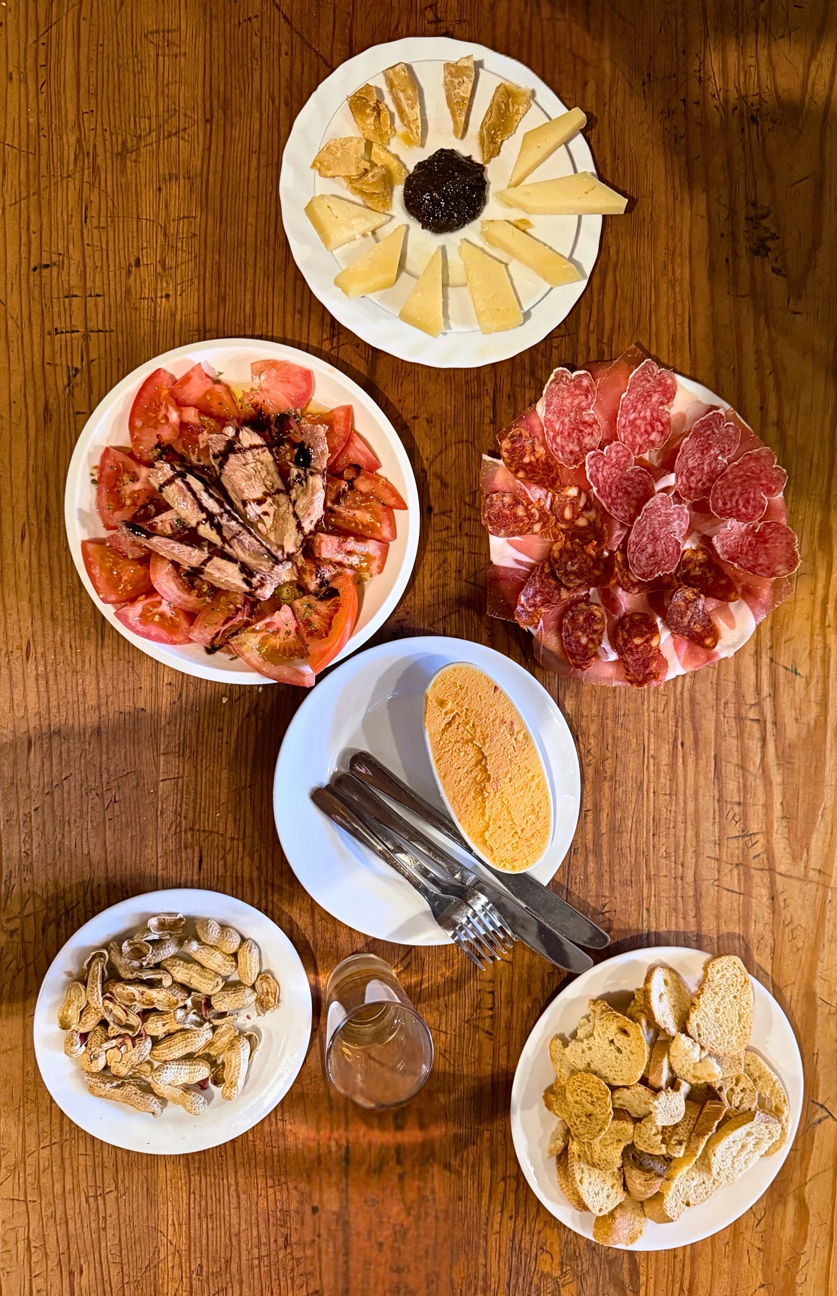 A table of cold tapas with cheese, tomatoes, tuna, cured meats, bread, and dip.