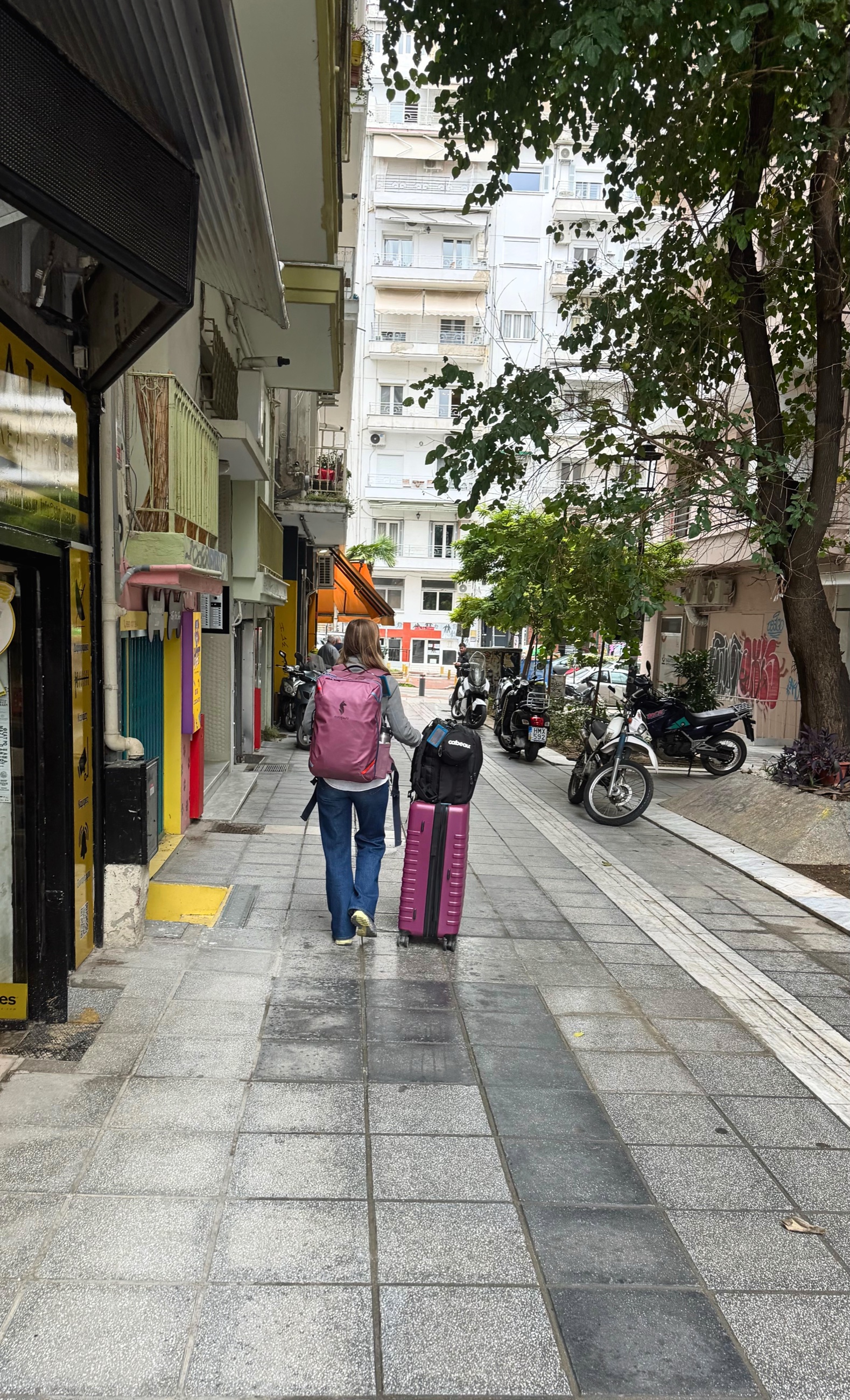 Stephanie walking with luggage on a Thessaloniki neighborhood street