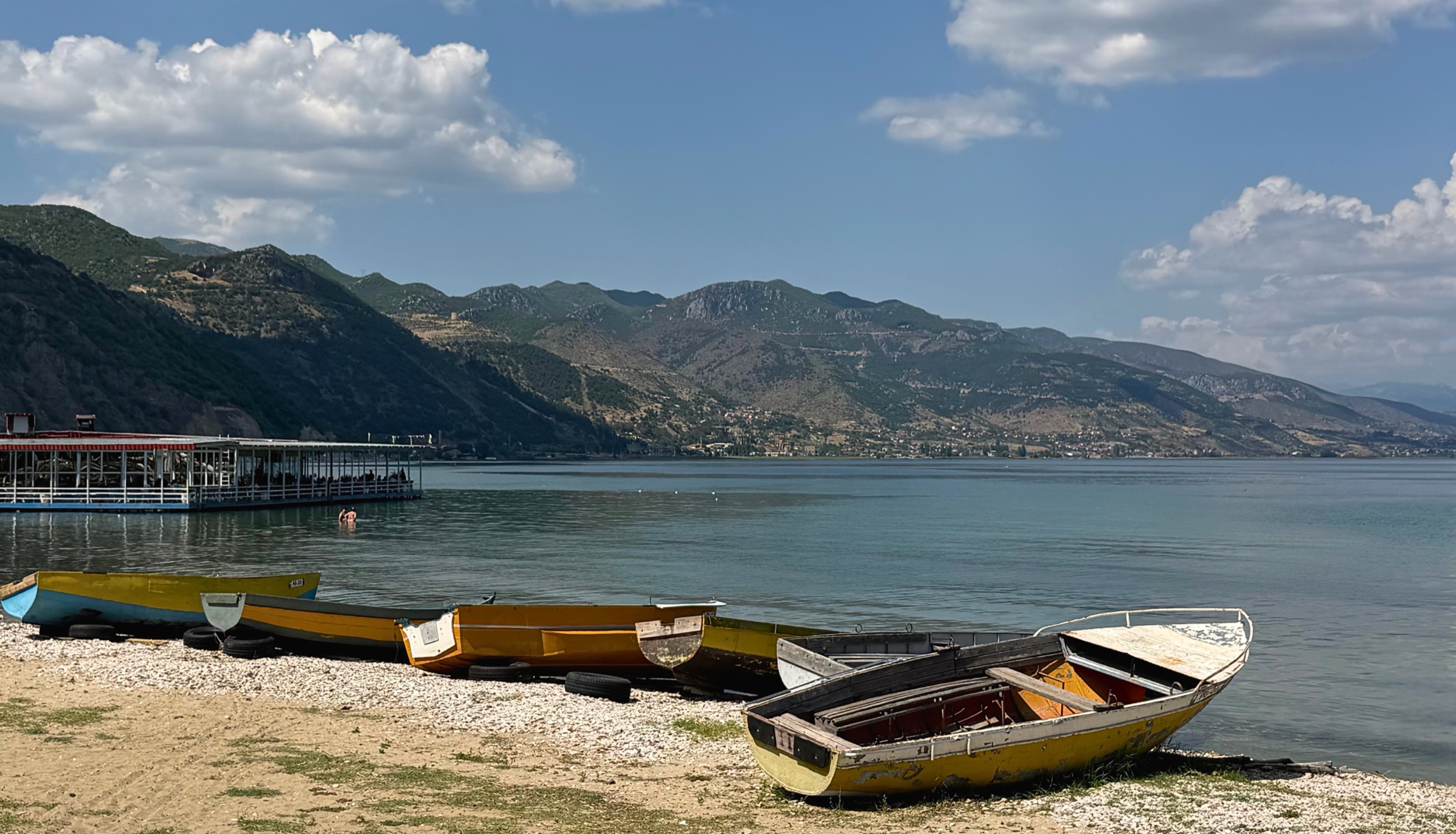 Weathered fishing boats on the shore of Lake Ohrid in Pogradec, Albania, with mountains across the water.