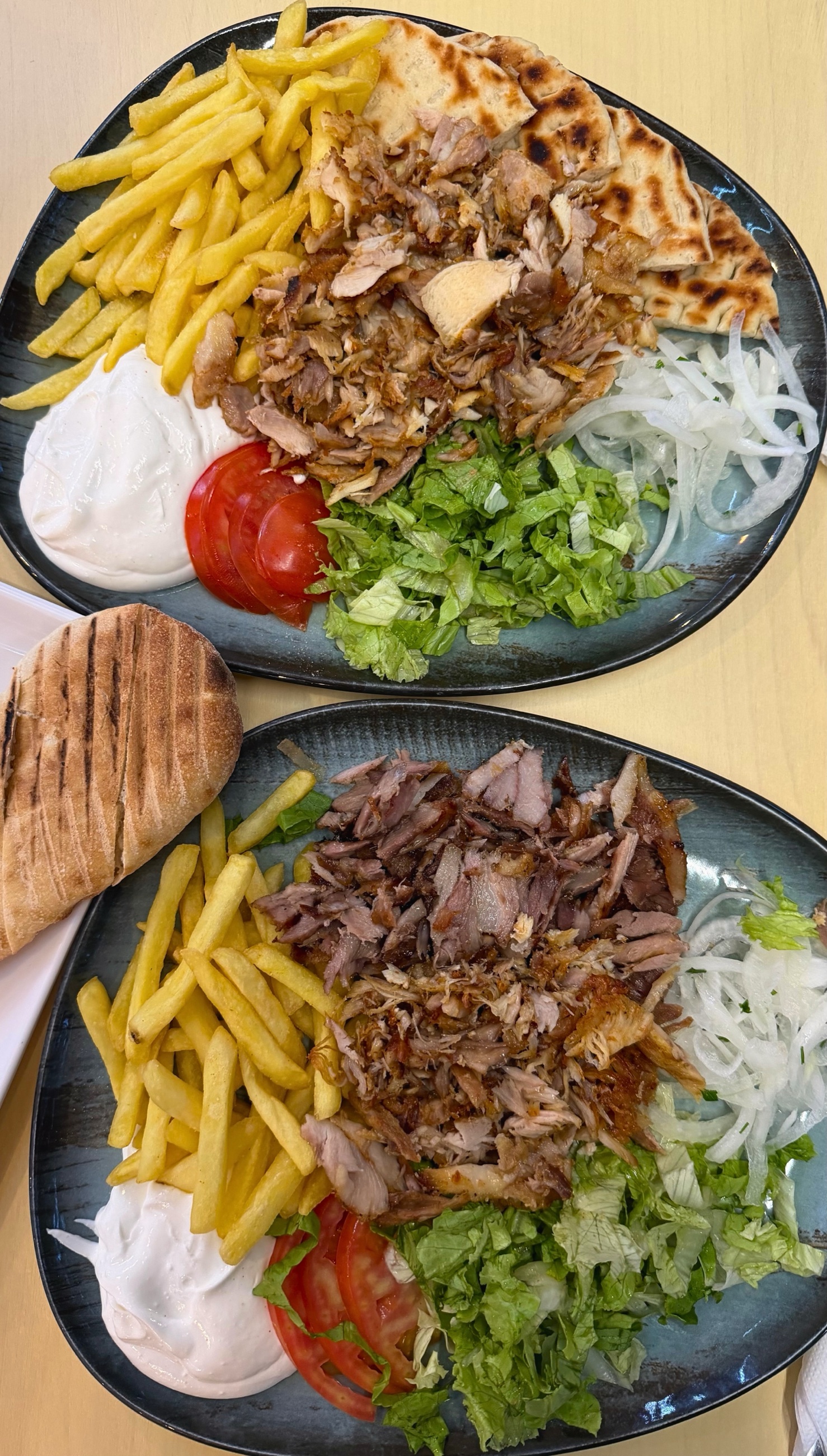 Open plate of Albanian sufllaqe with shaved meat, tomatoes, onions, lettuce, fries, pita, and yogurt sauce.