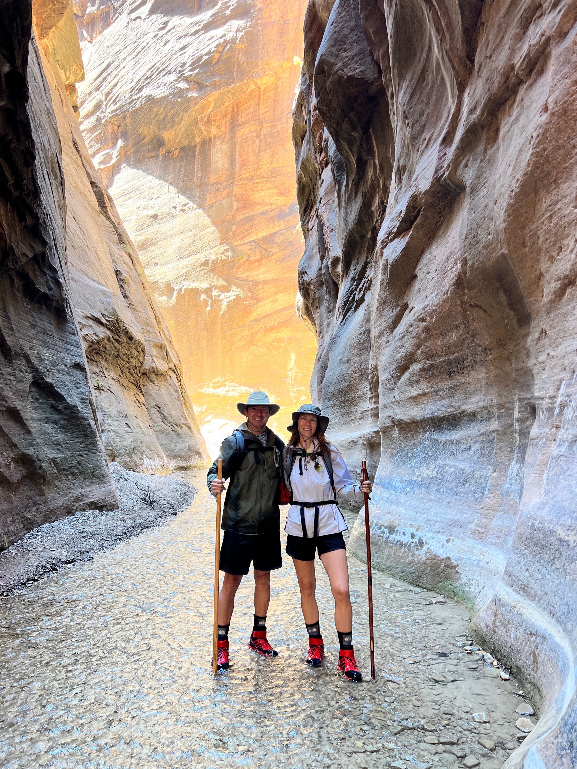 Morning light entering the Narrows in Zion National Park as hikers move through the Virgin River between canyon walls.